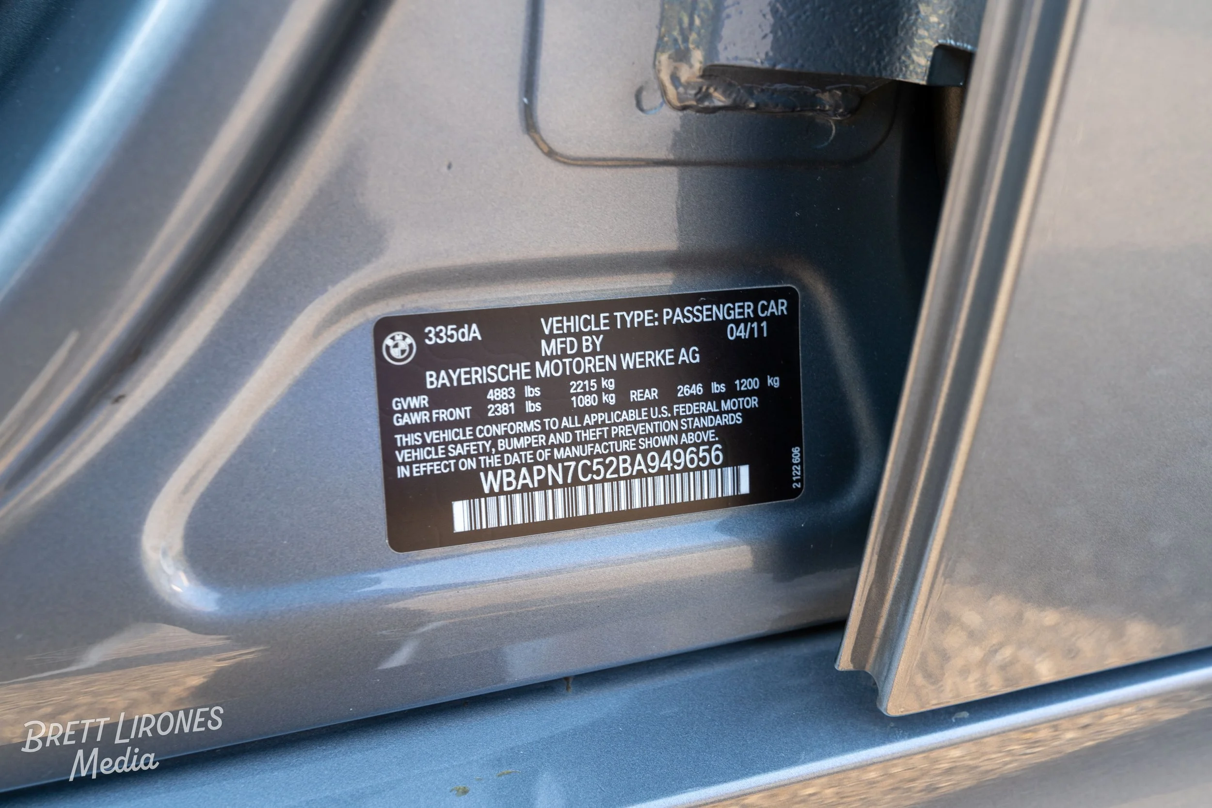 Vehicle identification label on car door frame showing manufacturer, vehicle type, manufacturing date, weight ratings, and a barcode.