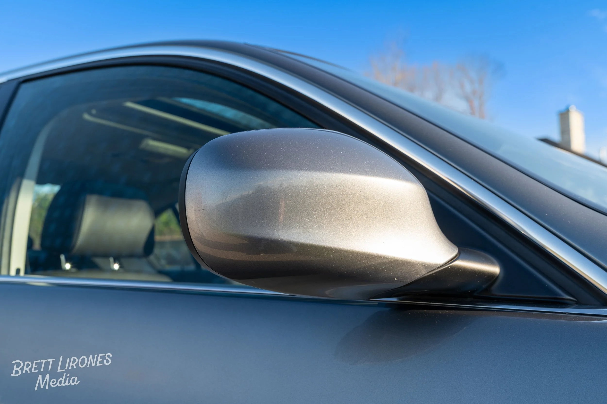 Close-up of a silver car's side mirror and part of the window with a blue sky background.
