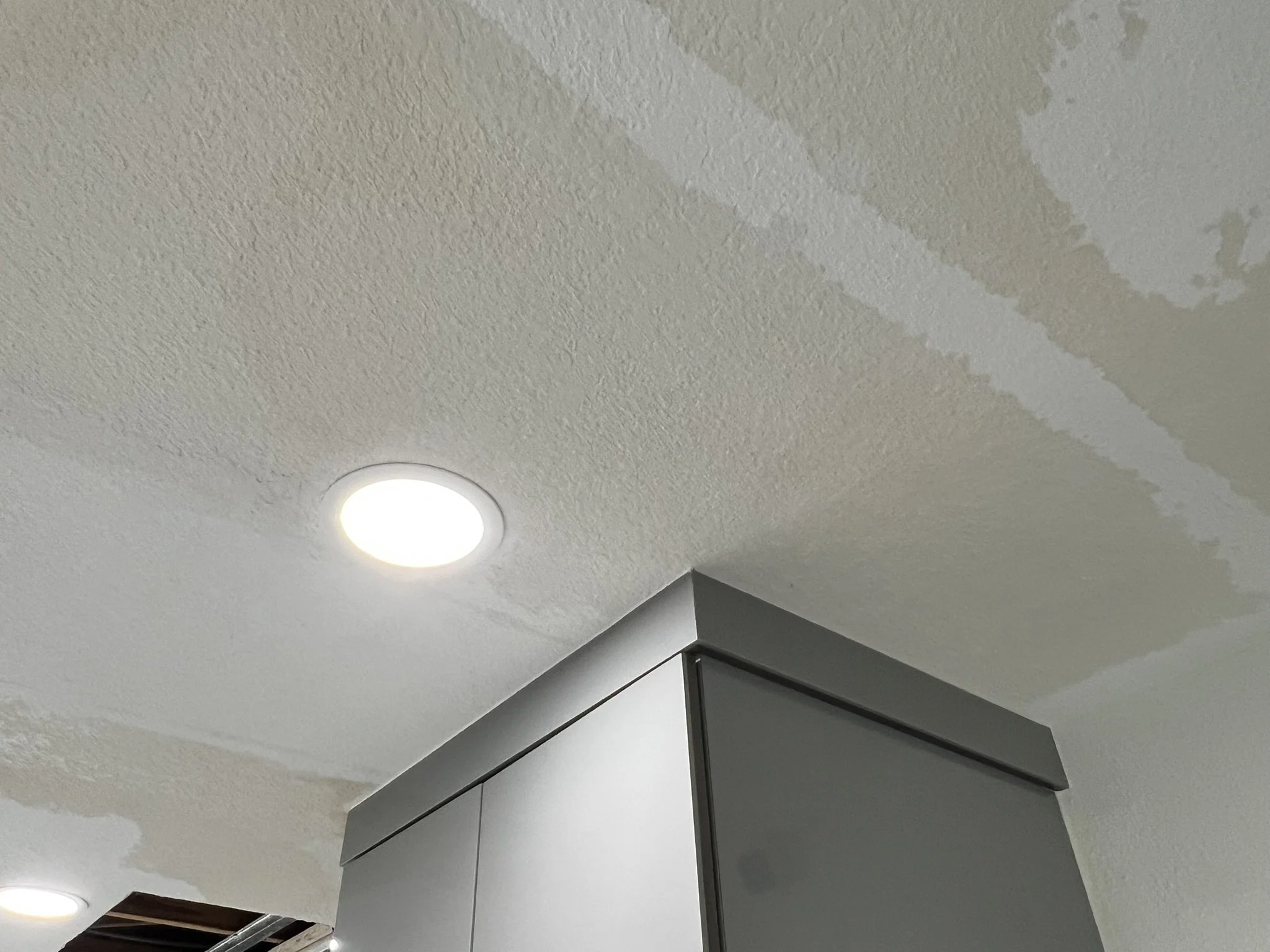 Ceiling with water damage and spots of paint peeling, a recessed light fixture, and a gray cabinet corner.