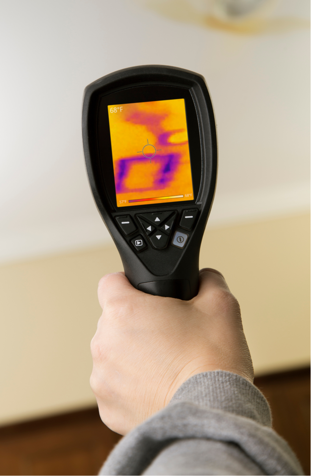 Hand holding a thermal imaging camera displaying a heat signature with warm colors on a wall.