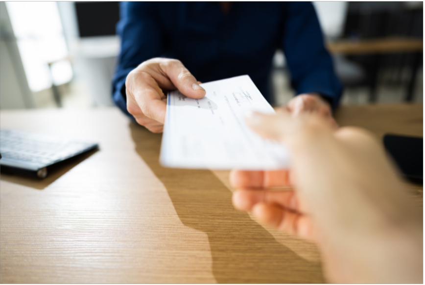 Person handing over a check to another person at a wooden desk.