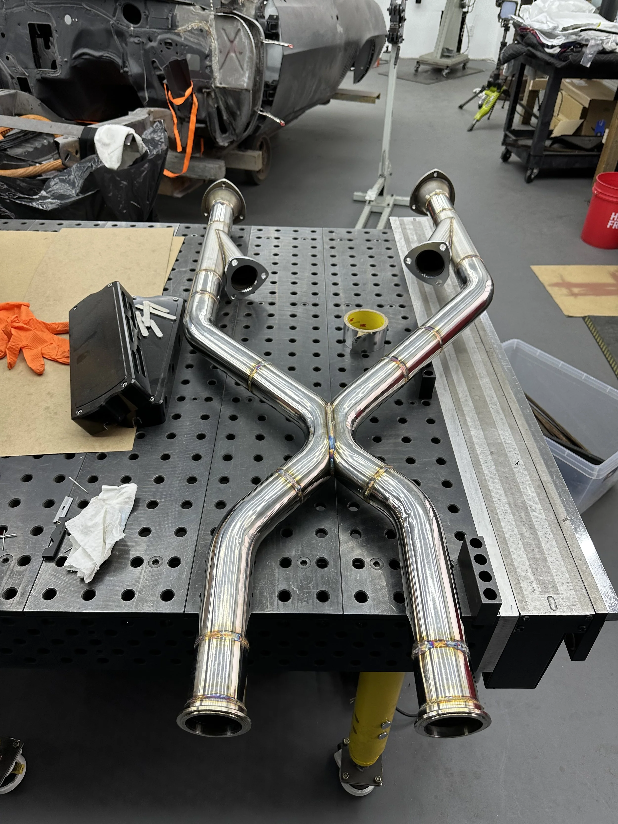 A polished stainless steel exhaust pipe with multiple bends on a workbench in a workshop.