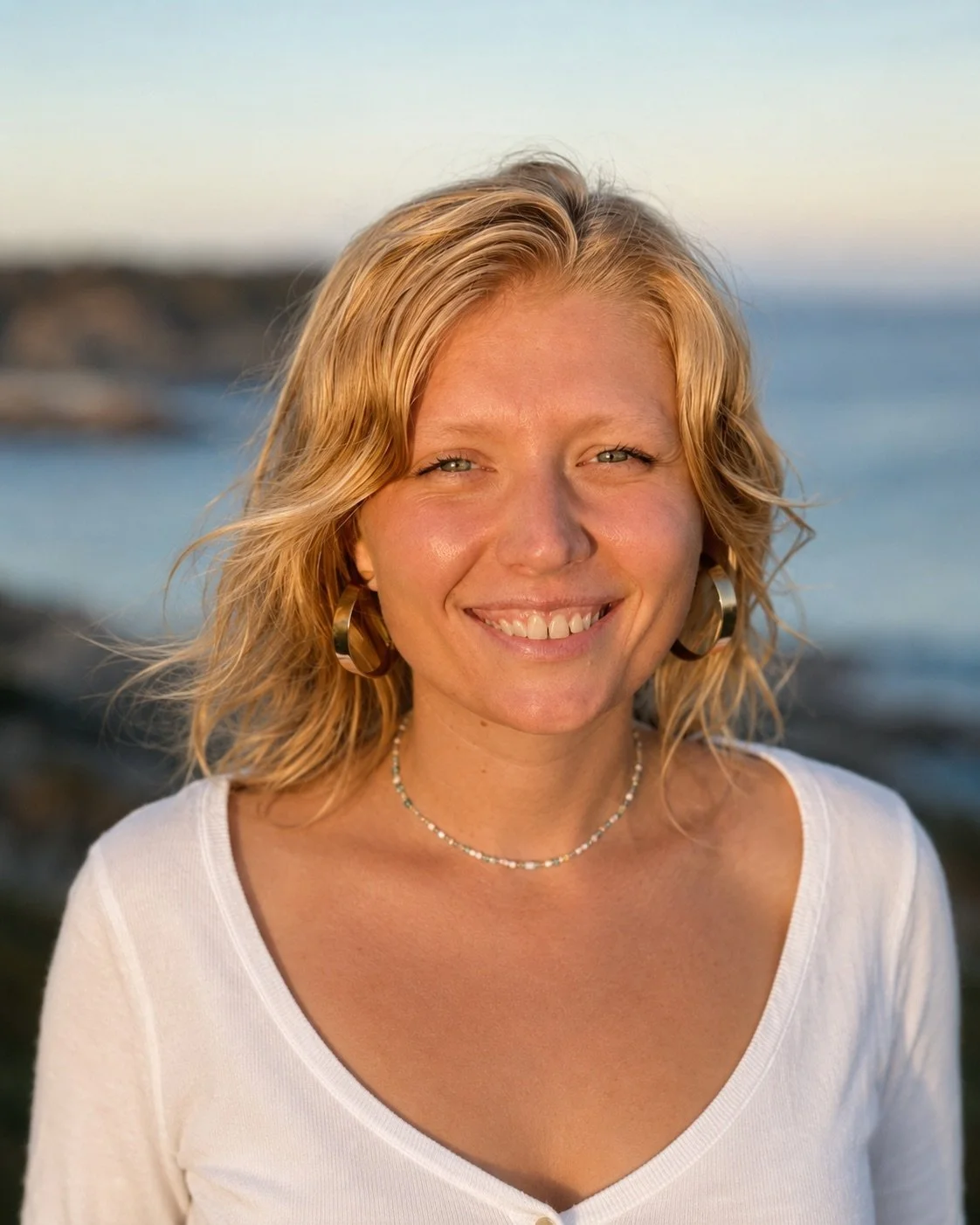 Ava Haag, founder of The Femme Explorer Studio, smiling by the ocean.
