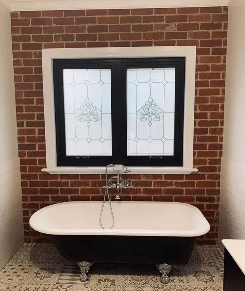 A bathtub with clawfoot style feet in a bathroom with brick wall behind a window with decorative glass.