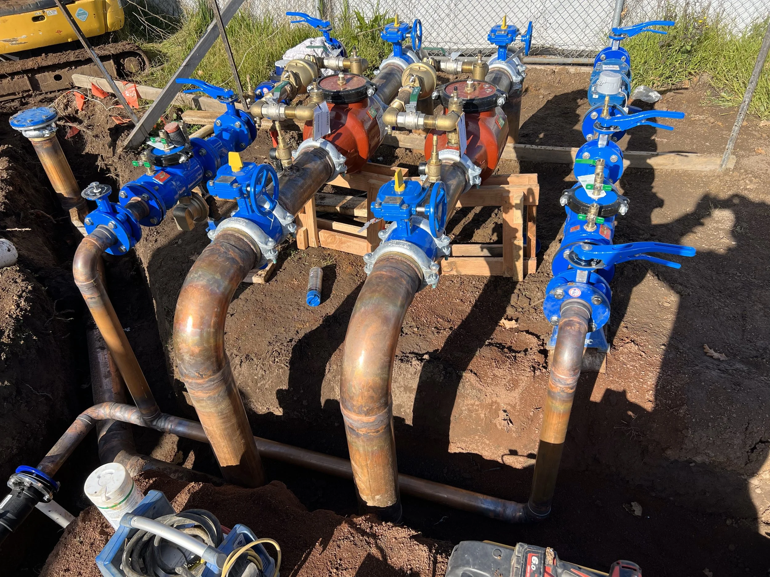 Underground water pipeline system with large copper pipes, blue valves, and pressure gauges installed in a construction site.