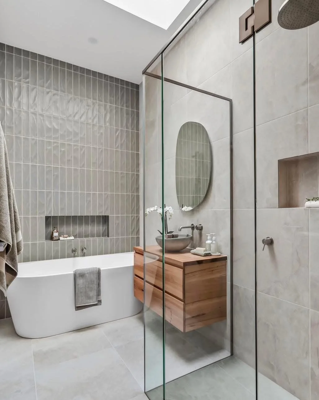 Modern bathroom with a bathtub, a wooden vanity with a vessel sink, a wall-mounted oval mirror, and a glass-enclosed shower area.