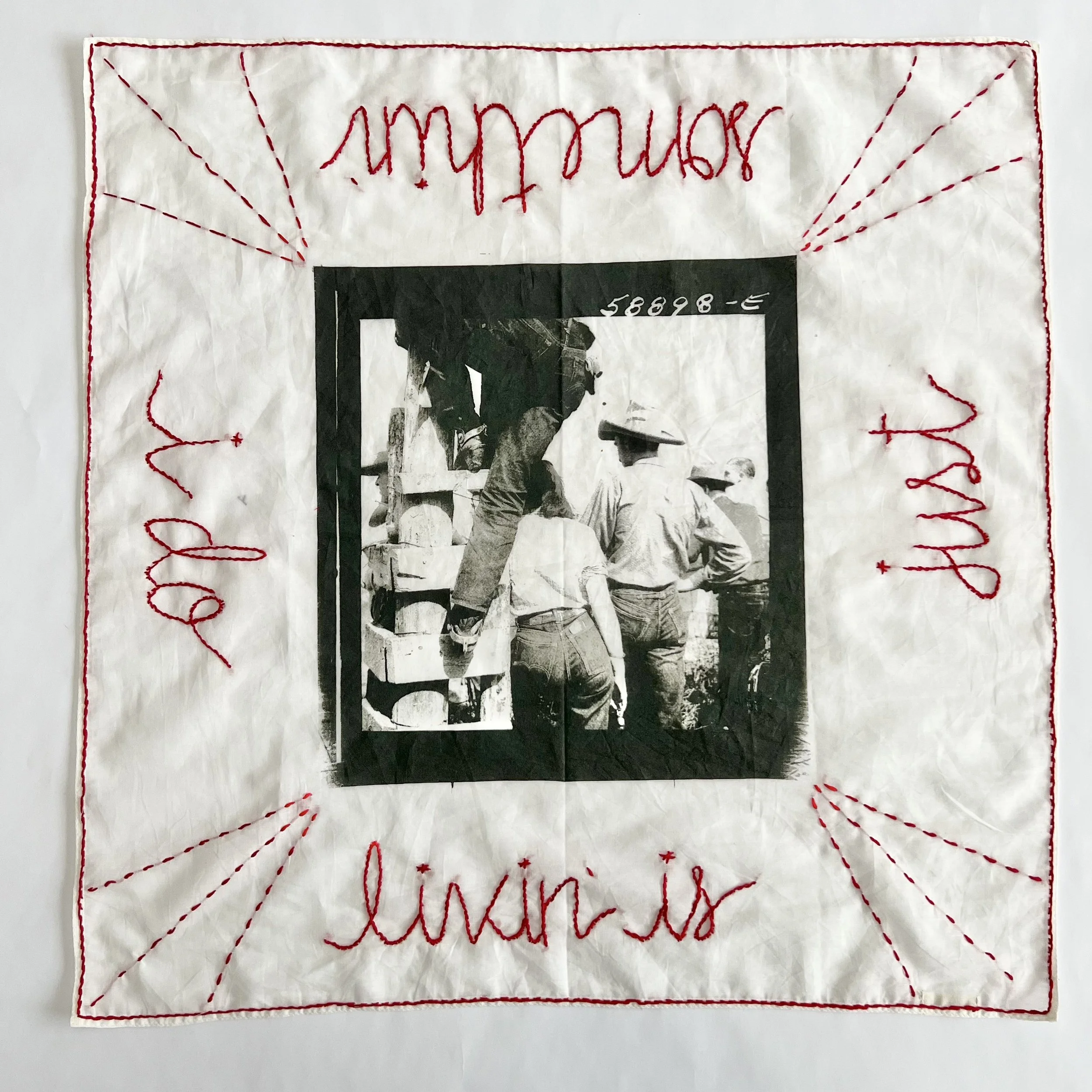 A fabric square with red embroidered words and a black and white photo in the center. The words say 'Learning' at the top, '.in is' at the bottom, 'and' on the left, and 'the' on the right. The photo depicts several people, including one standing on a ladder, with some wearing hats, engaged in construction or similar activity.