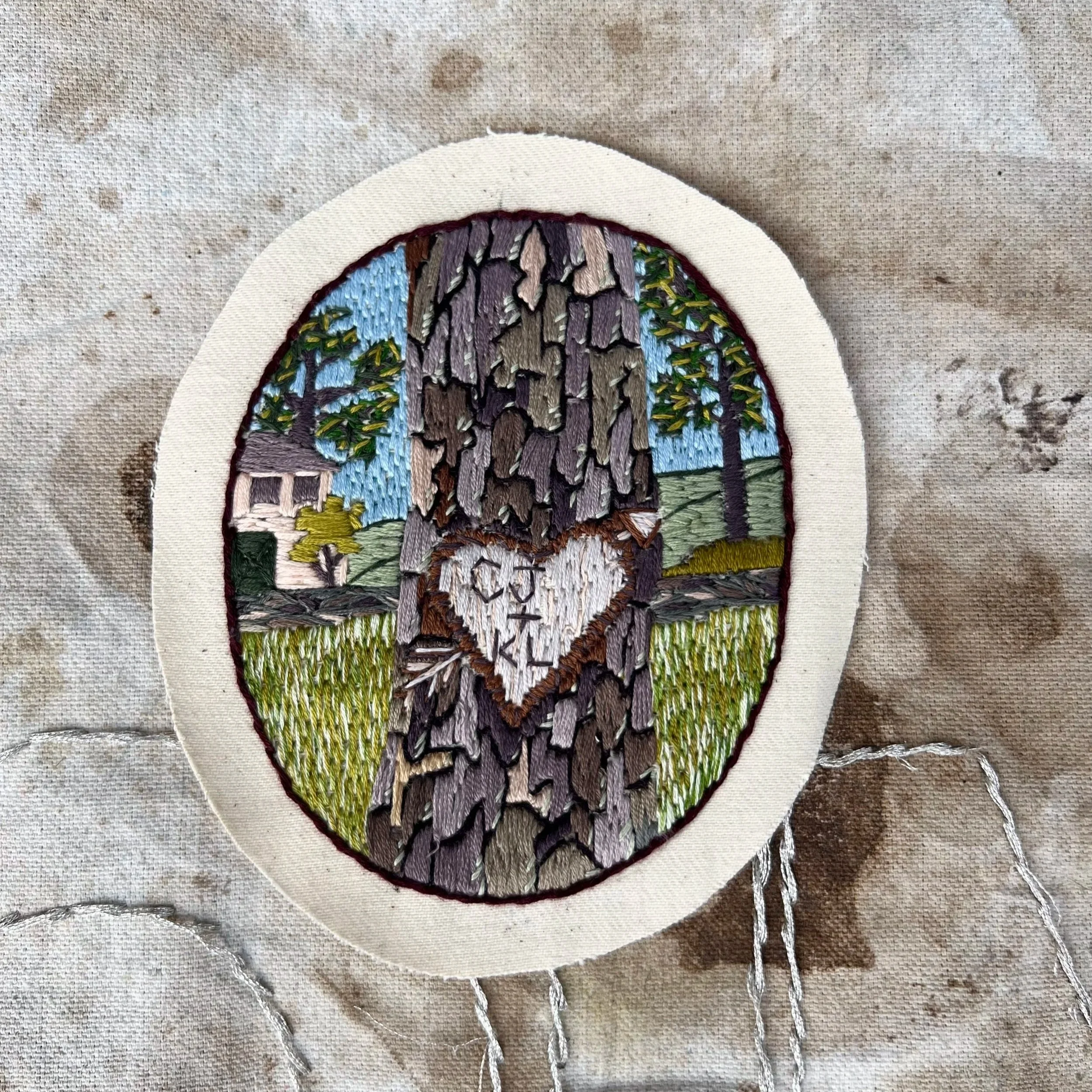 Hand-embroidered arbor glyph patch inspired by carved initials in tree bark, stitched on artist canvas as a wearable patch.