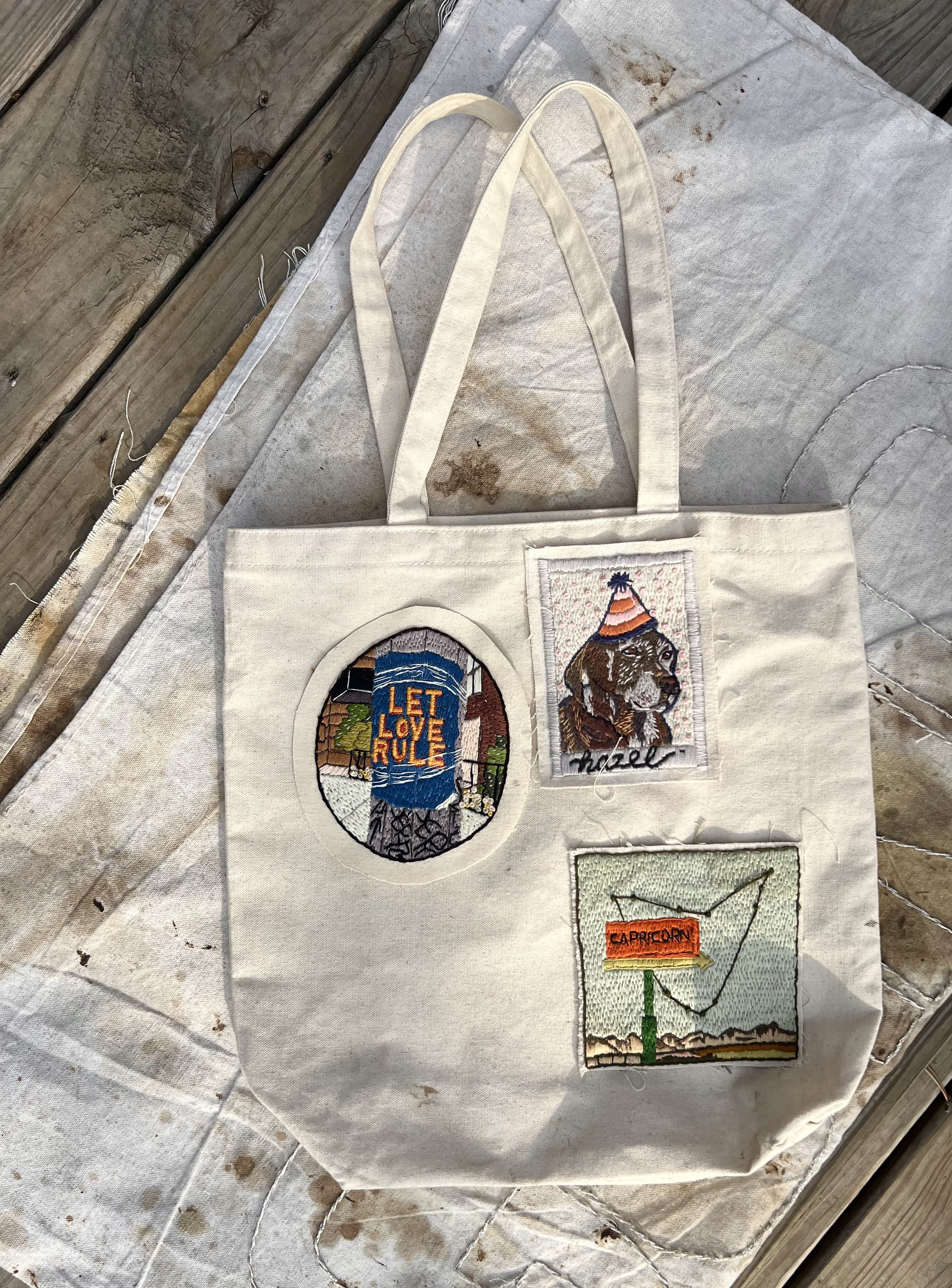 Canvas tote bag featuring Let Love Rule patch alongside custom pet portrait and zodiac patches, designed to be collected over time.
