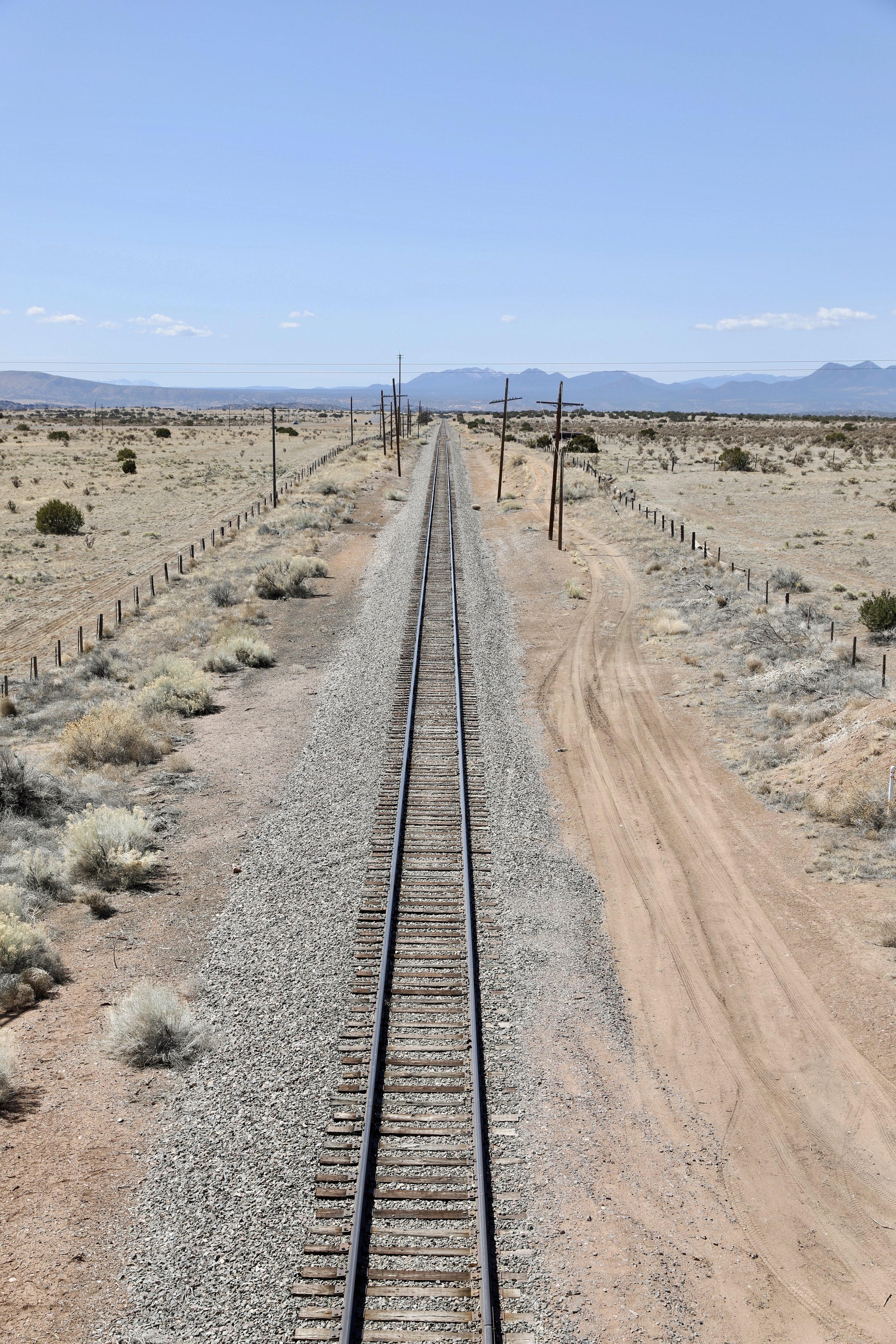 Railroad track running through a desert landscape with mountains in the distance under a blue sky.