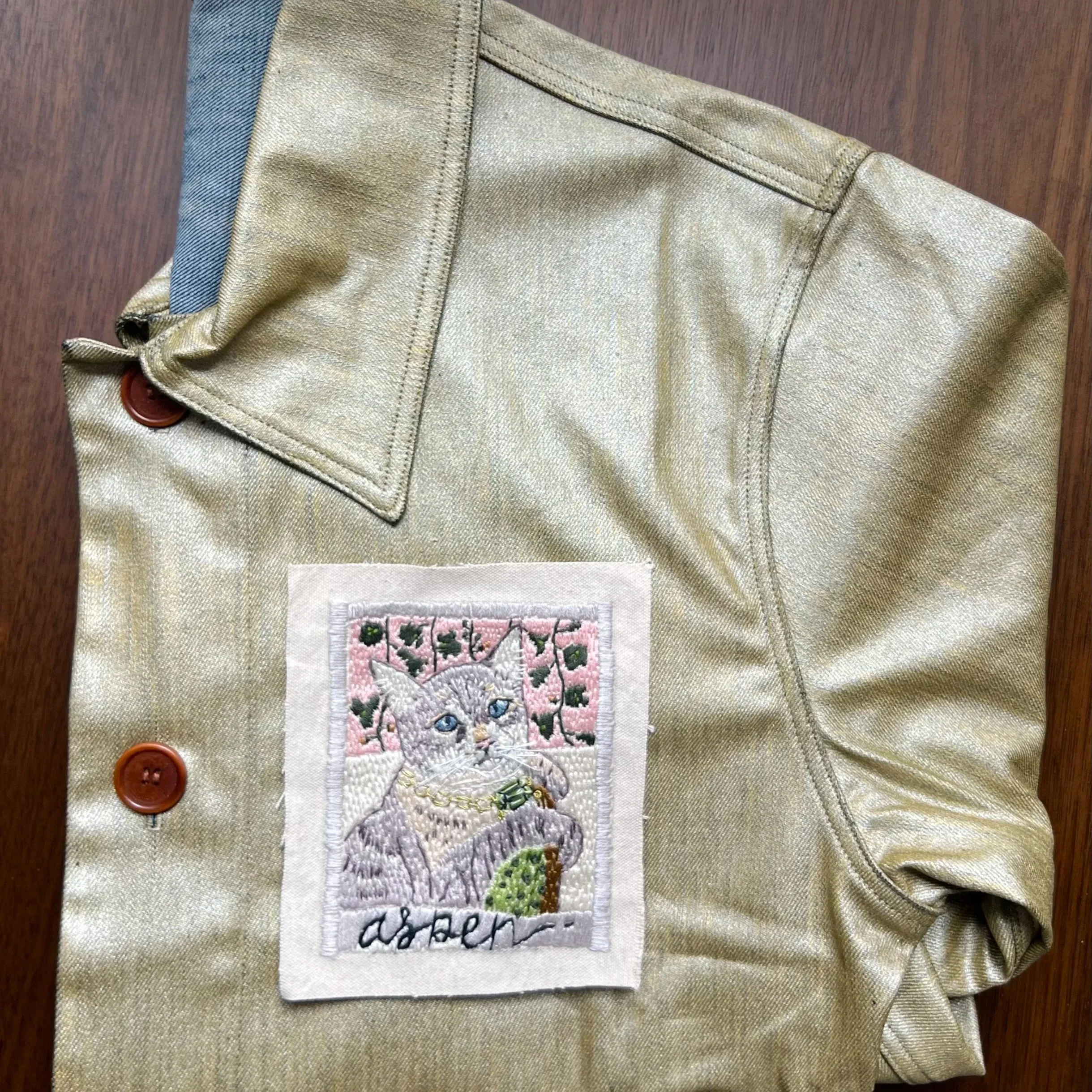 A custom gold waxed denim jacket, with a hand-embroidered portrait of the cat aspen sewn on the breast.