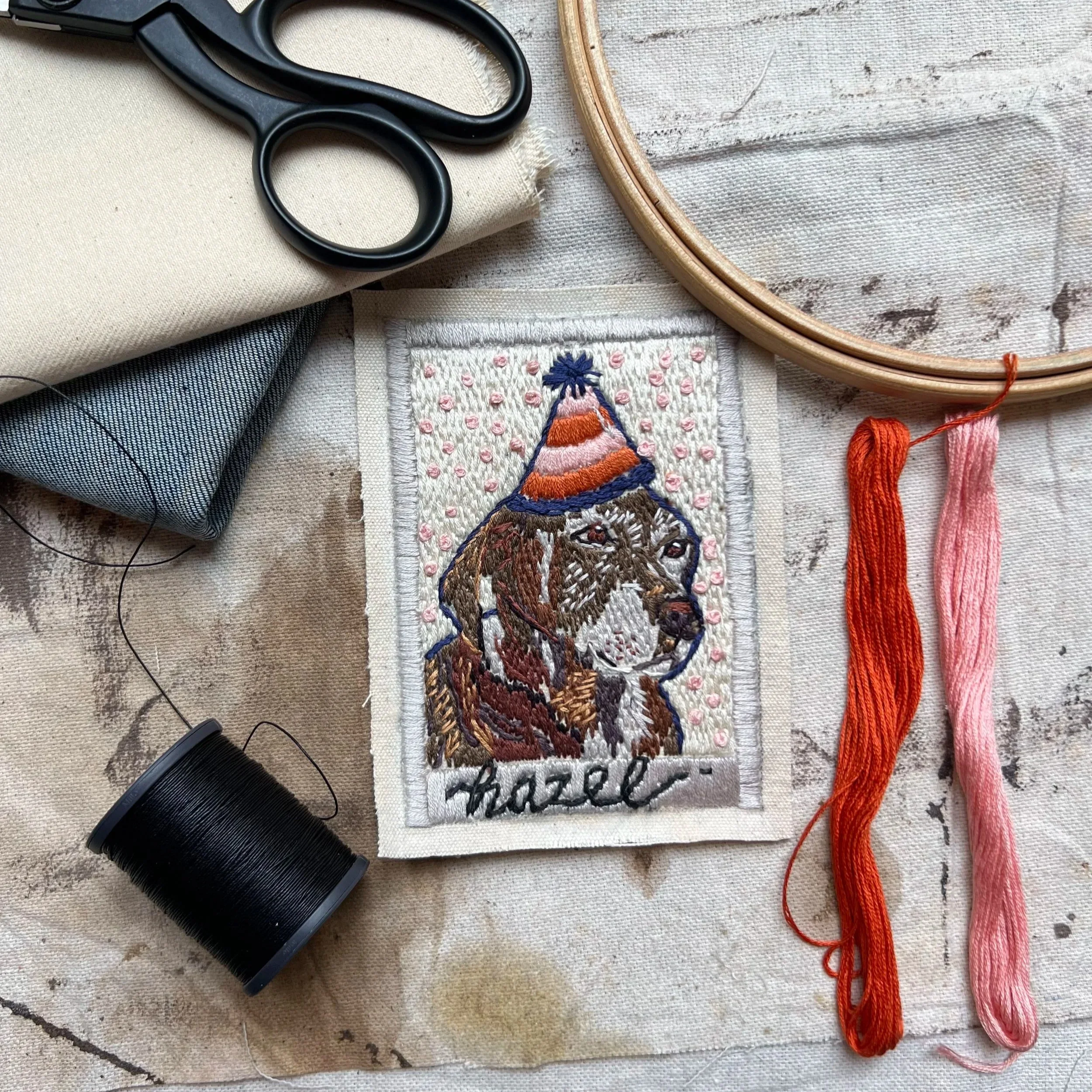 A brown dog in a party hat. A custom hand stitched portrait of a dog against a confetti background.