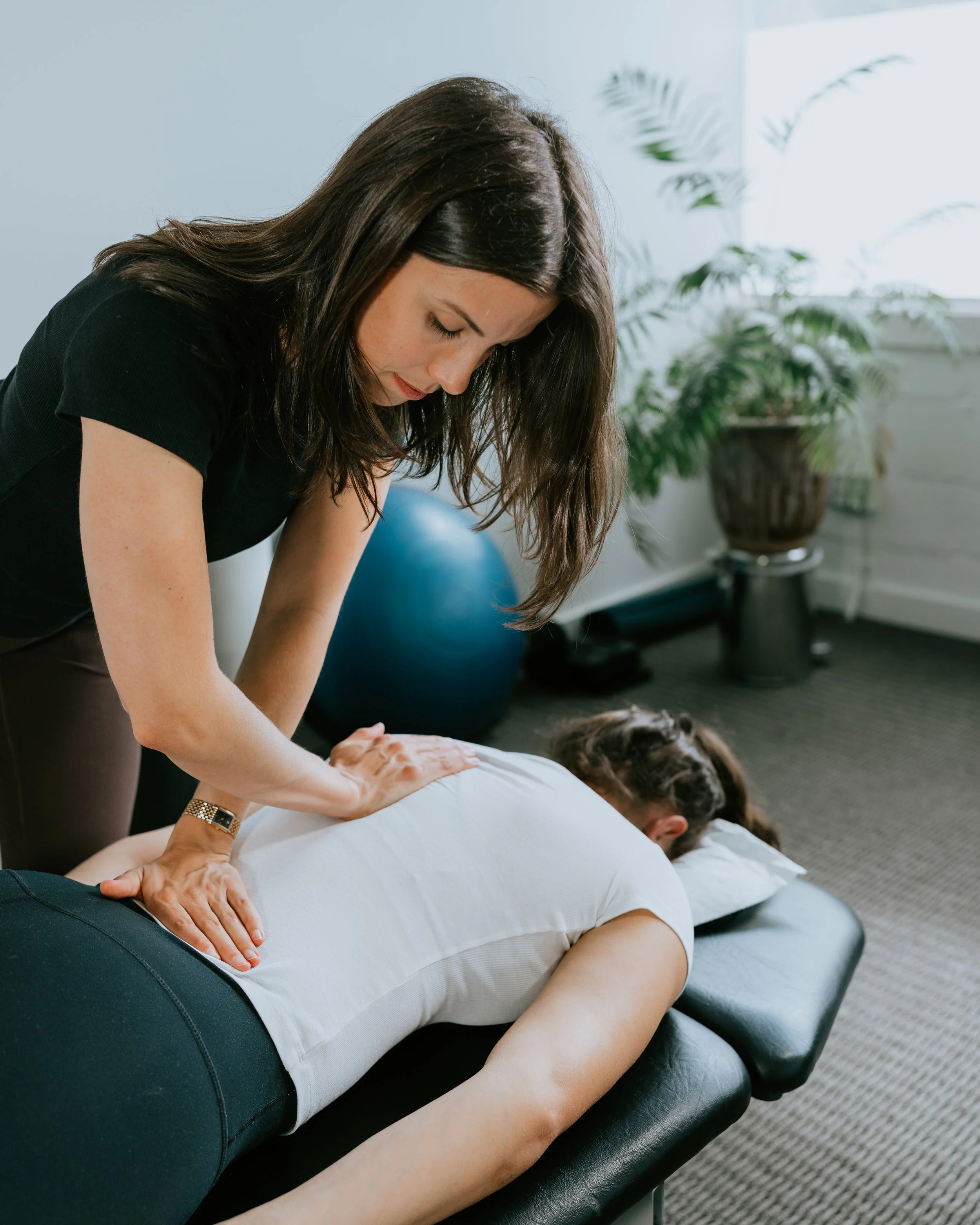 Chiropractor performing an adjustment on a woman lying face down on a chiropractic table in a therapy room.
