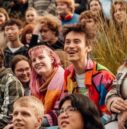 Group of young people sitting outdoors, smiling and enjoying a gathering.