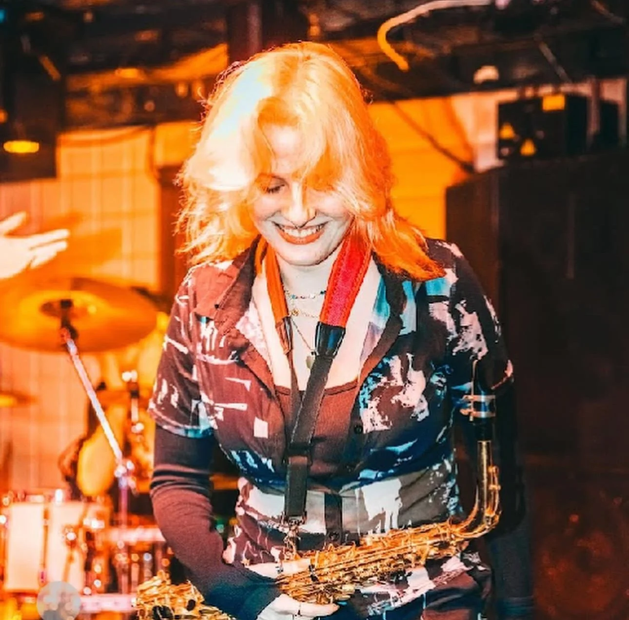 A woman with blonde hair playing the saxophone on stage during a performance, smiling and enjoying the moment.