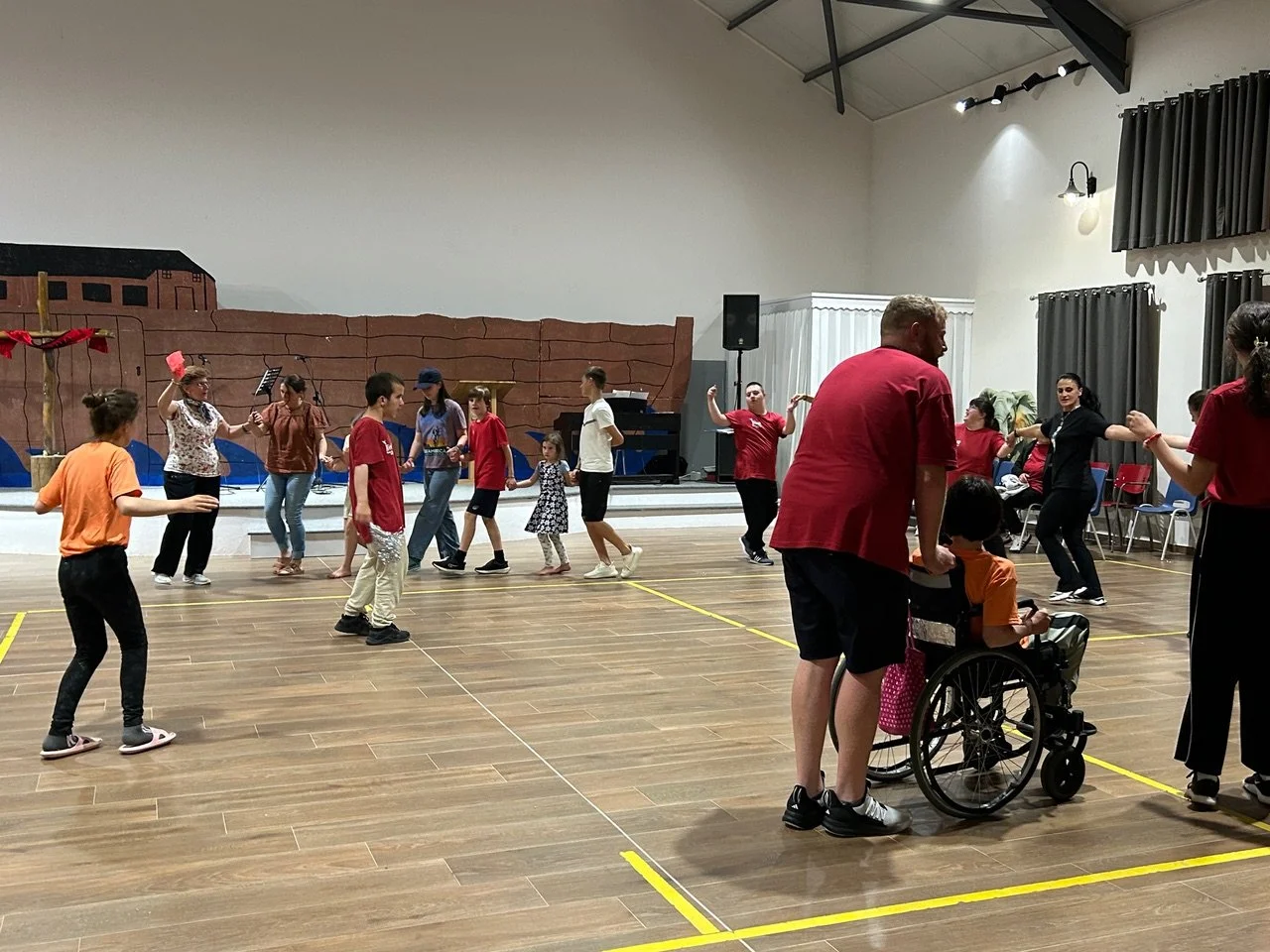 People dancing and enjoying a group dance session in a spacious hall with a stage backdrop and musical equipment.