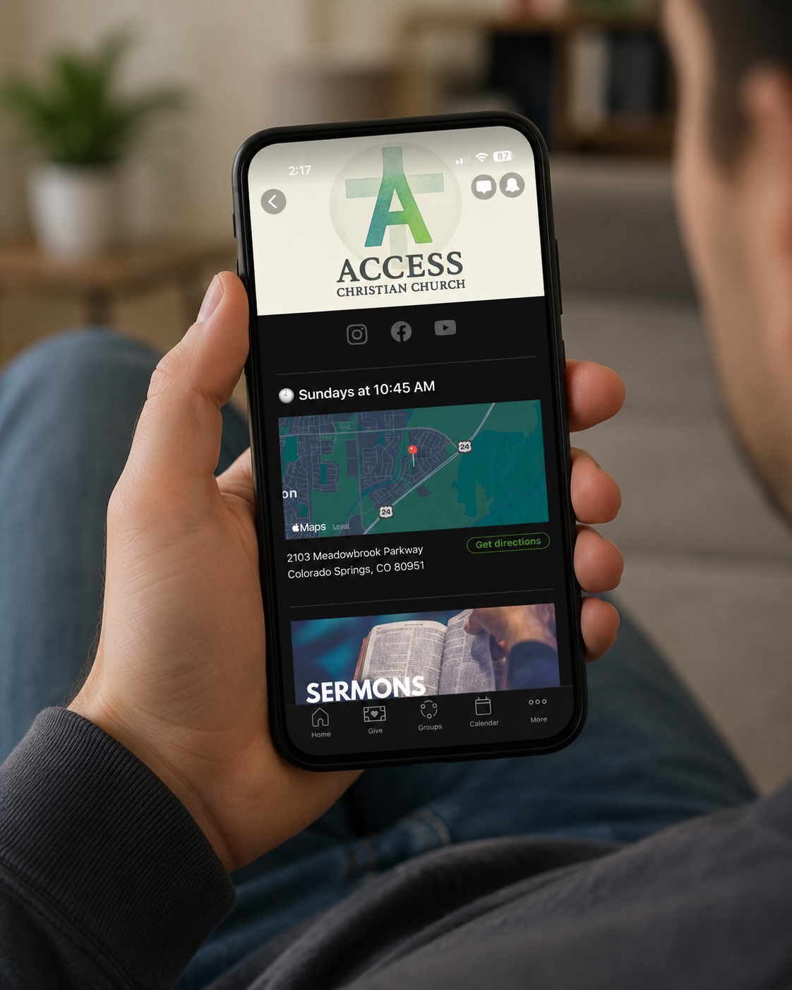 Person holding a smartphone displaying an app for Access Christian Church, showing service times, location, and social media links.