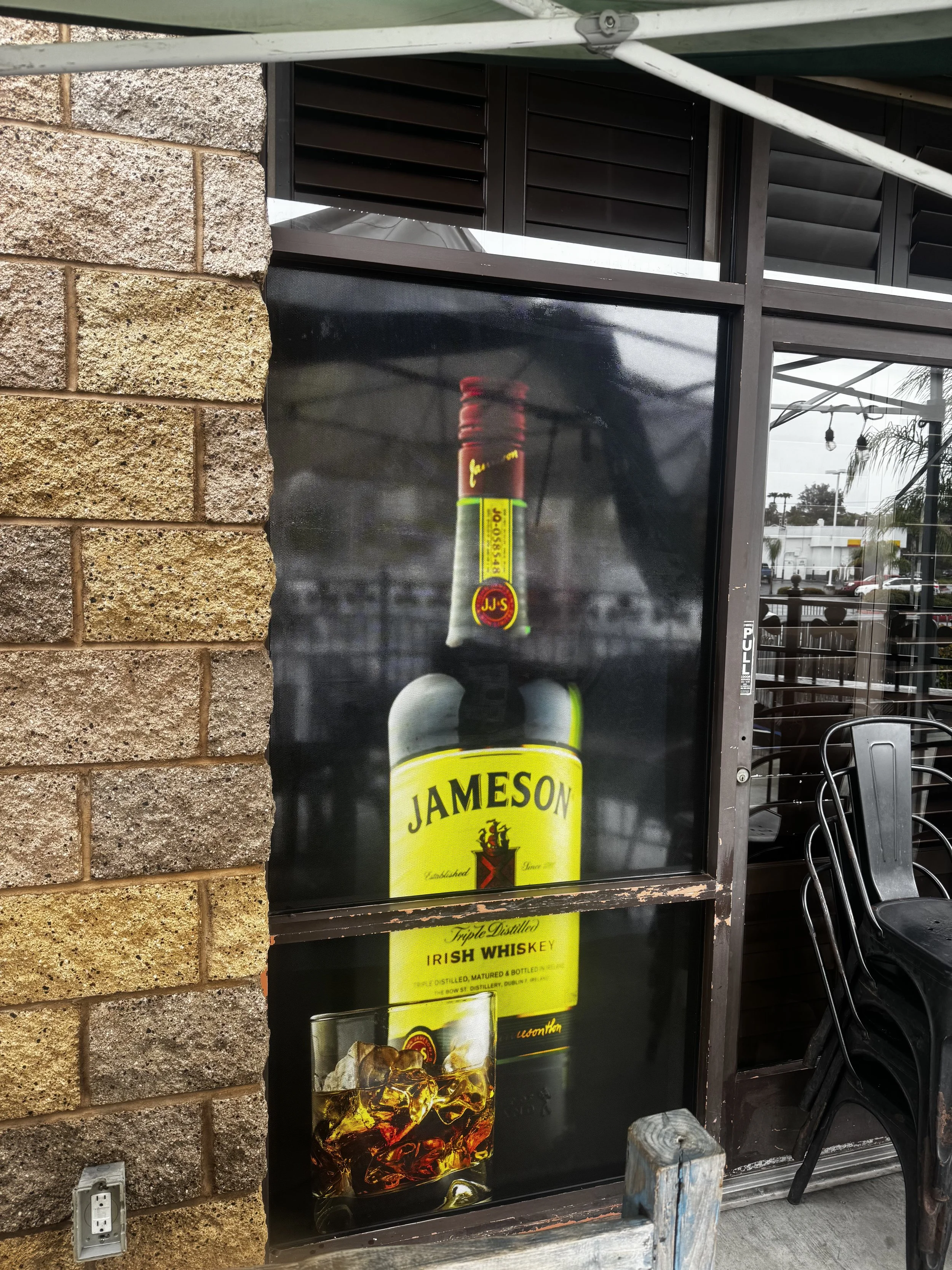 Poster of Jameson Irish Whiskey featuring a bottle and a glass of whiskey with ice, mounted on a window outside a building.