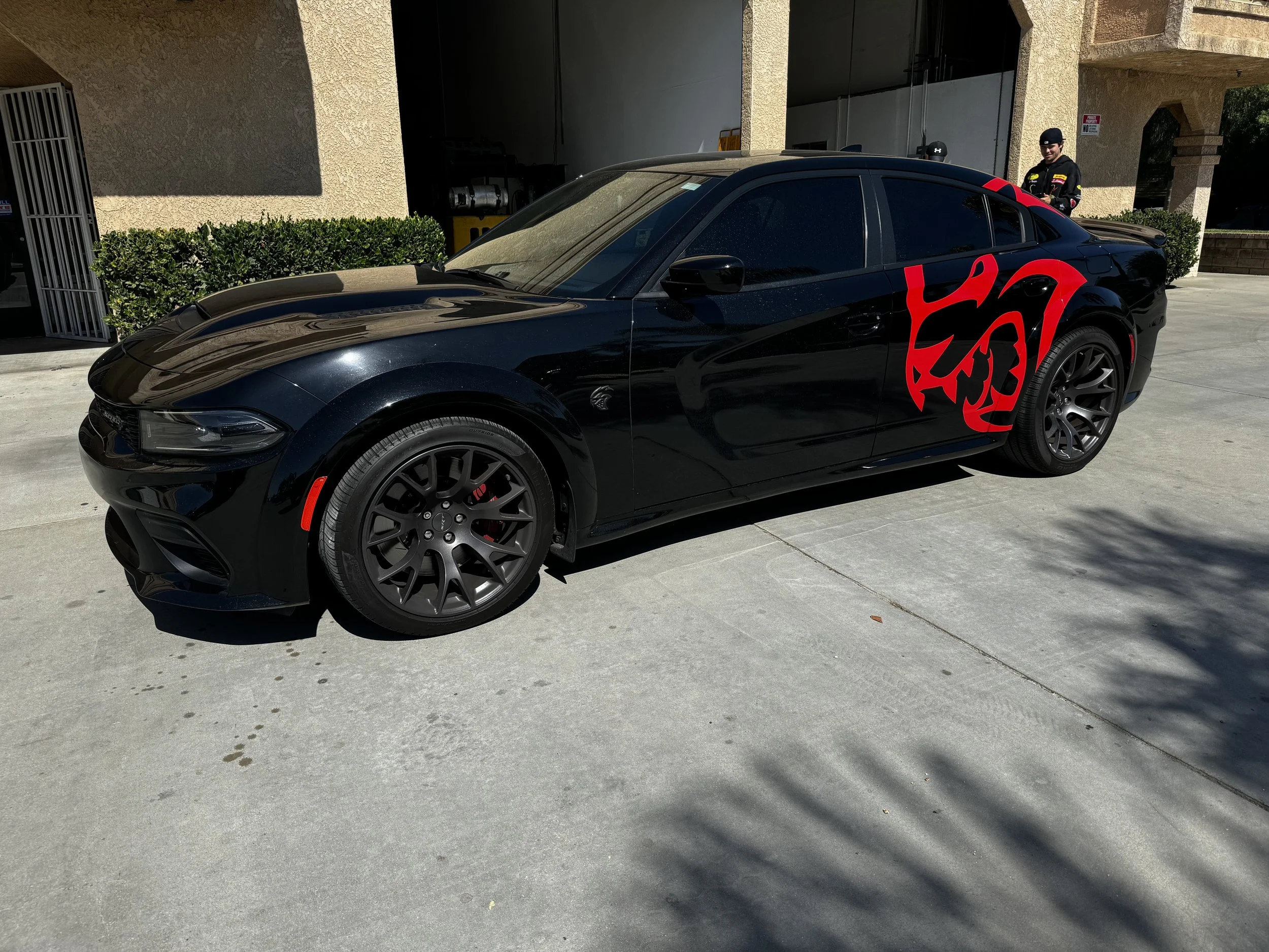 Black sports car with red dragon design on side, parked outside building, two people in black uniforms standing near the car.
