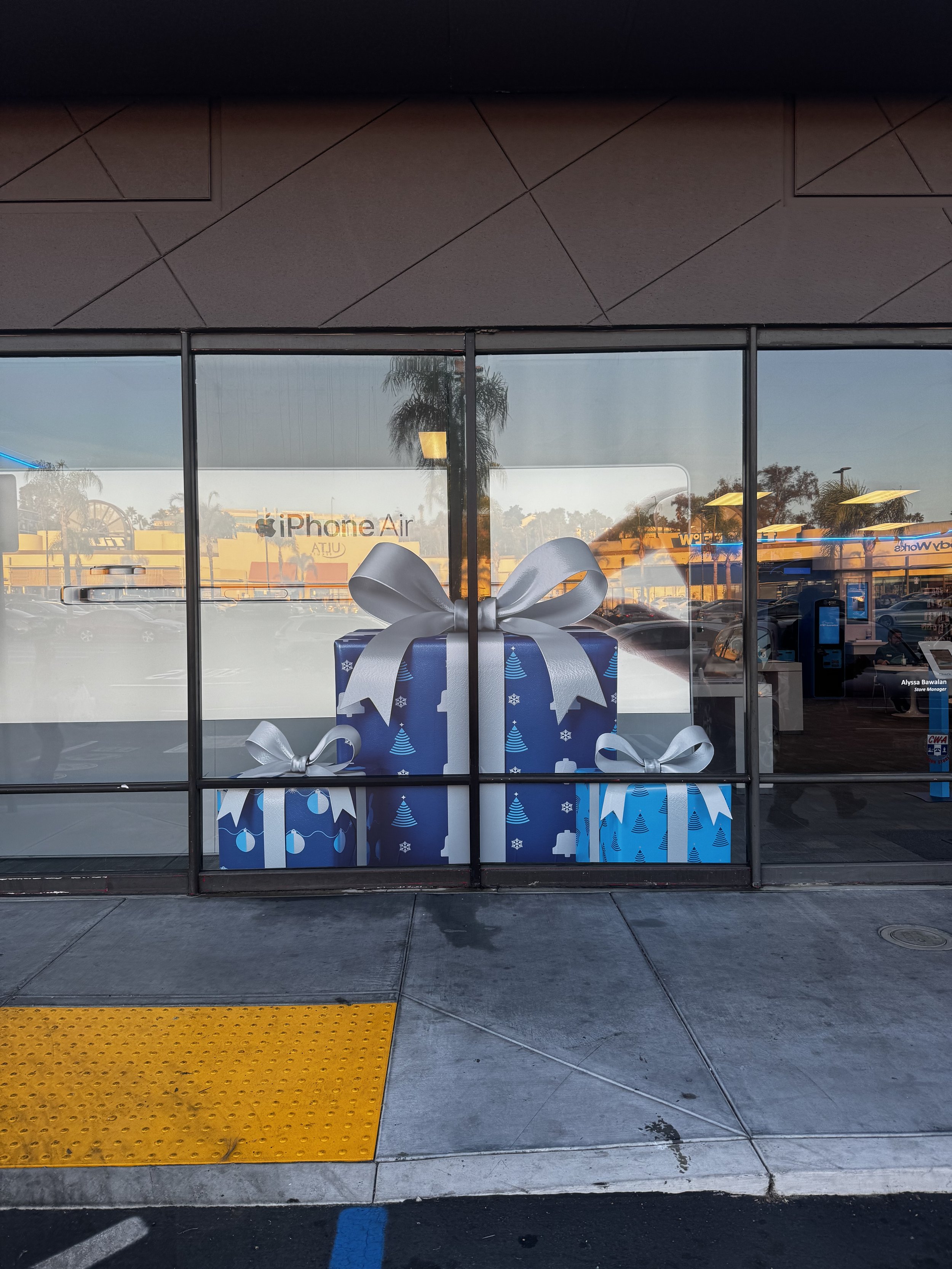 Store window display with large, wrapped gift boxes decorated with holiday motifs and silver ribbons in a retail store.