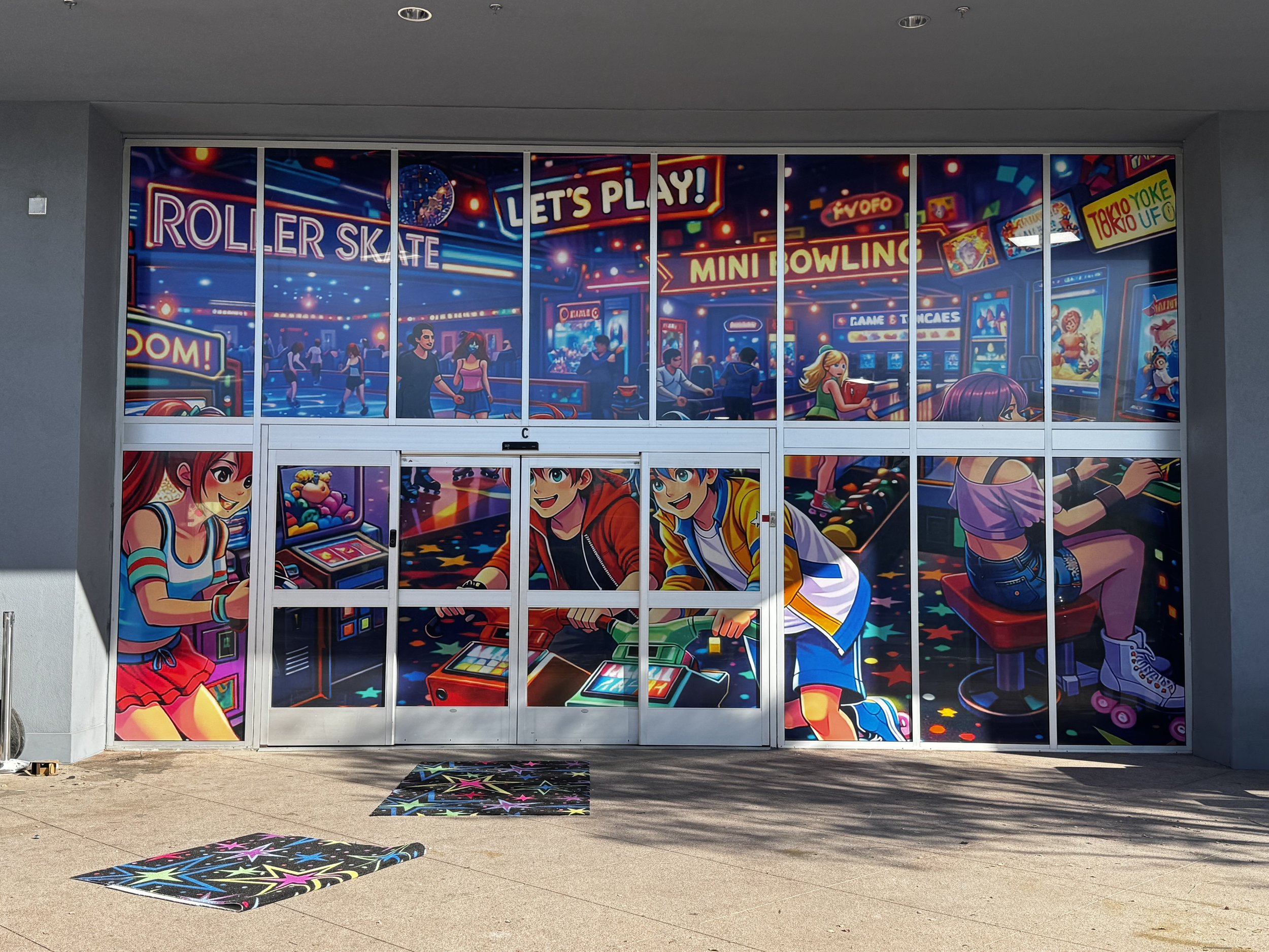 Colorful mural of an arcade game room with characters playing games like pinball and skateboarding, and signs that say "ROLLER SKATE," "LET'S PLAY!," and "MINI BOWLING."