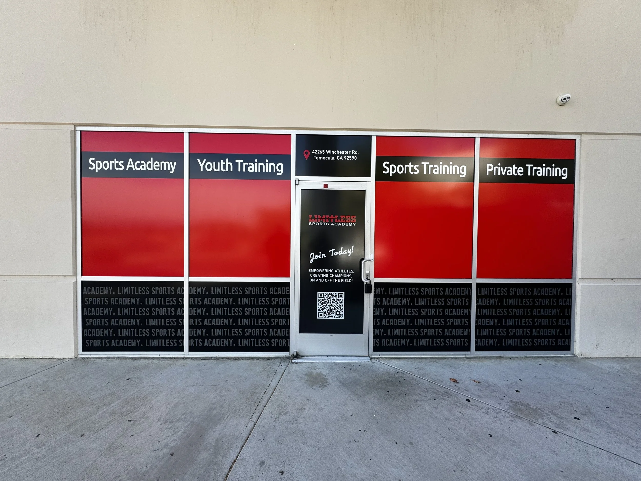 Storefront window advertising sports academy and training services, including youth and private training, with a door in the center showing the address 42265 Winchester Rd, Temecula, CA 92590, and a QR code at the bottom.