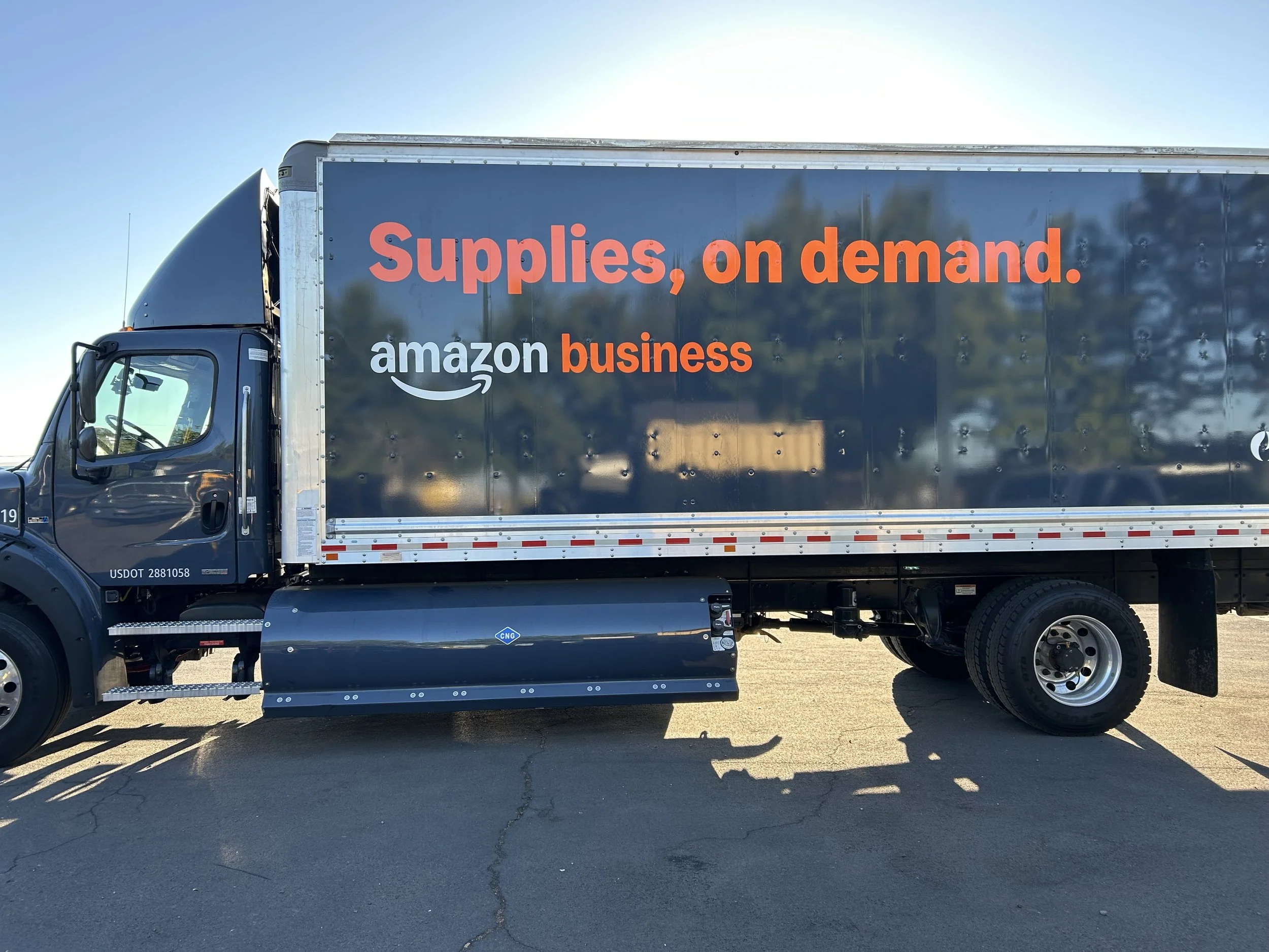A large black Amazon delivery truck with the text 'Supplies, on demand.' and 'amazon business' in orange and white lettering on the side.