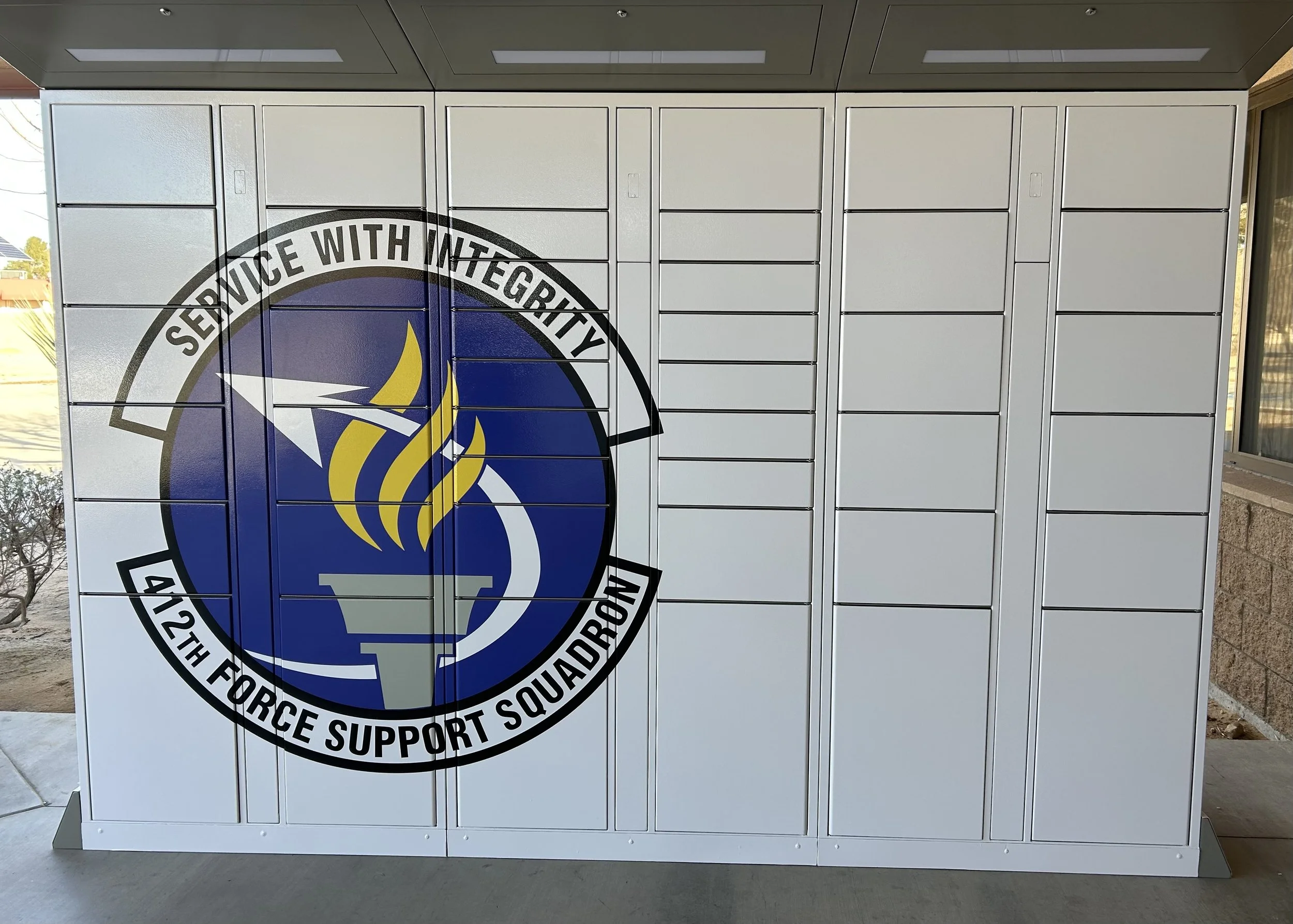 A set of white lockers with a large logo on the front that says "Service with Integrity, 42th Force Support Squadron," featuring a torch with yellow flames and a blue background.