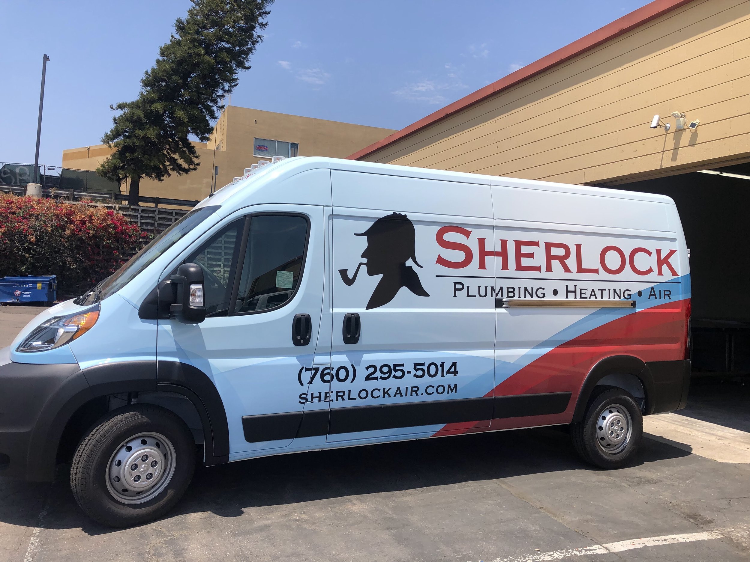Sherlock Plumbing, Heating, and Air service van parked in a lot with a beige building, trees, and blue sky in the background.