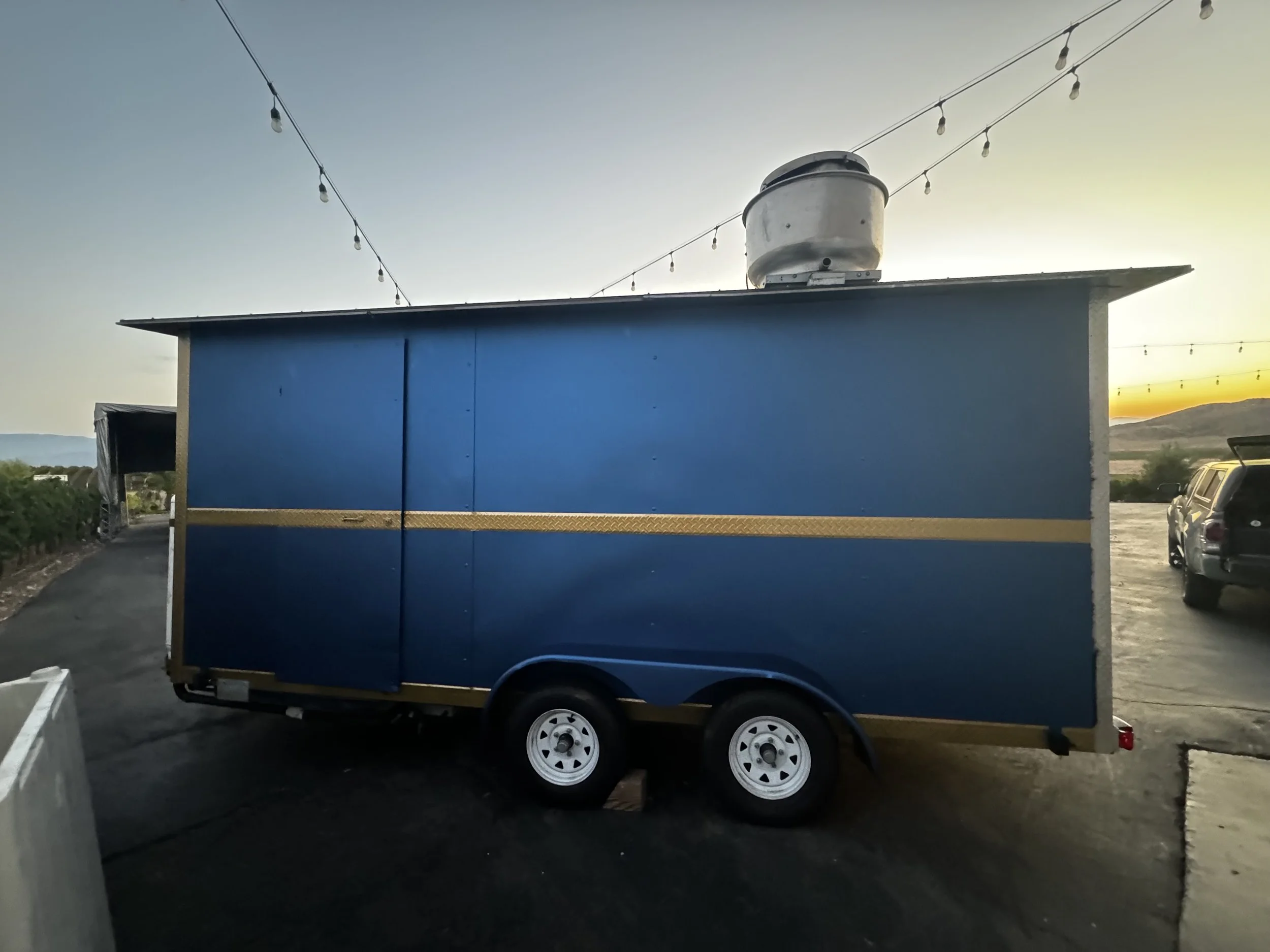 Blue food truck with a gold stripe at sunset.