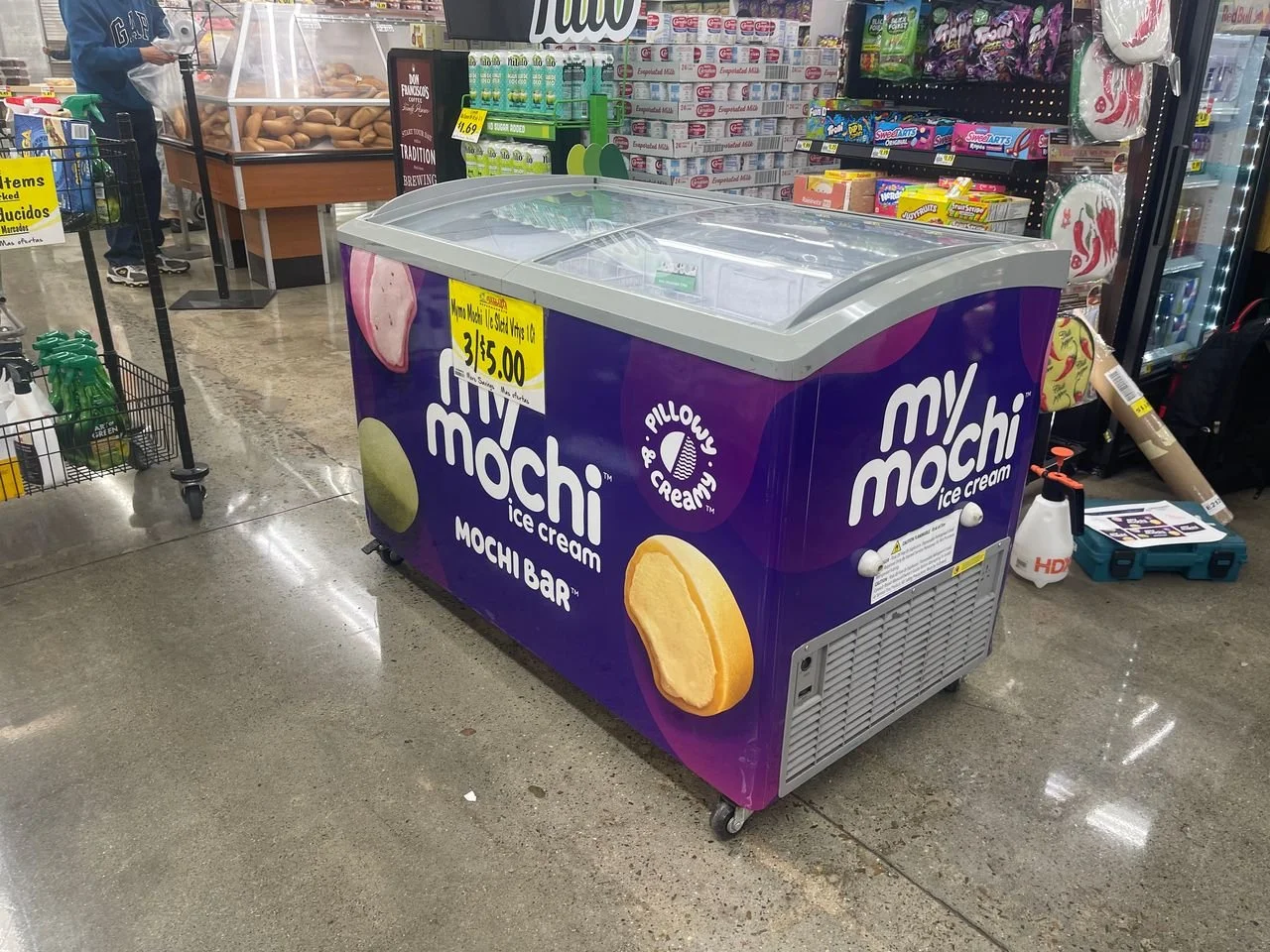 A purple My Mochi ice cream freezer with pictures of mochi bars on it, located in a supermarket aisle.