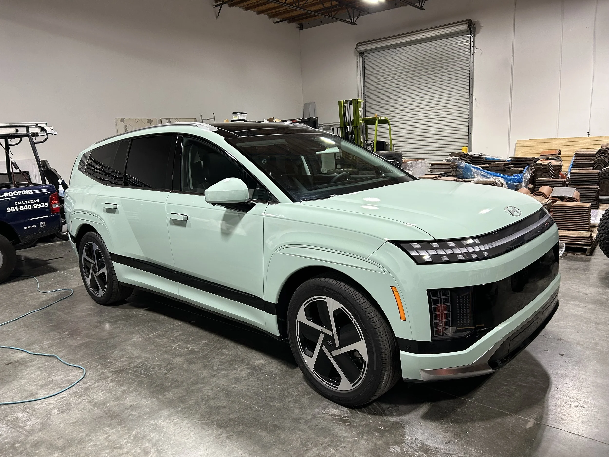 A mint green Hyundai electric SUV inside a warehouse, surrounded by building materials and equipment.
