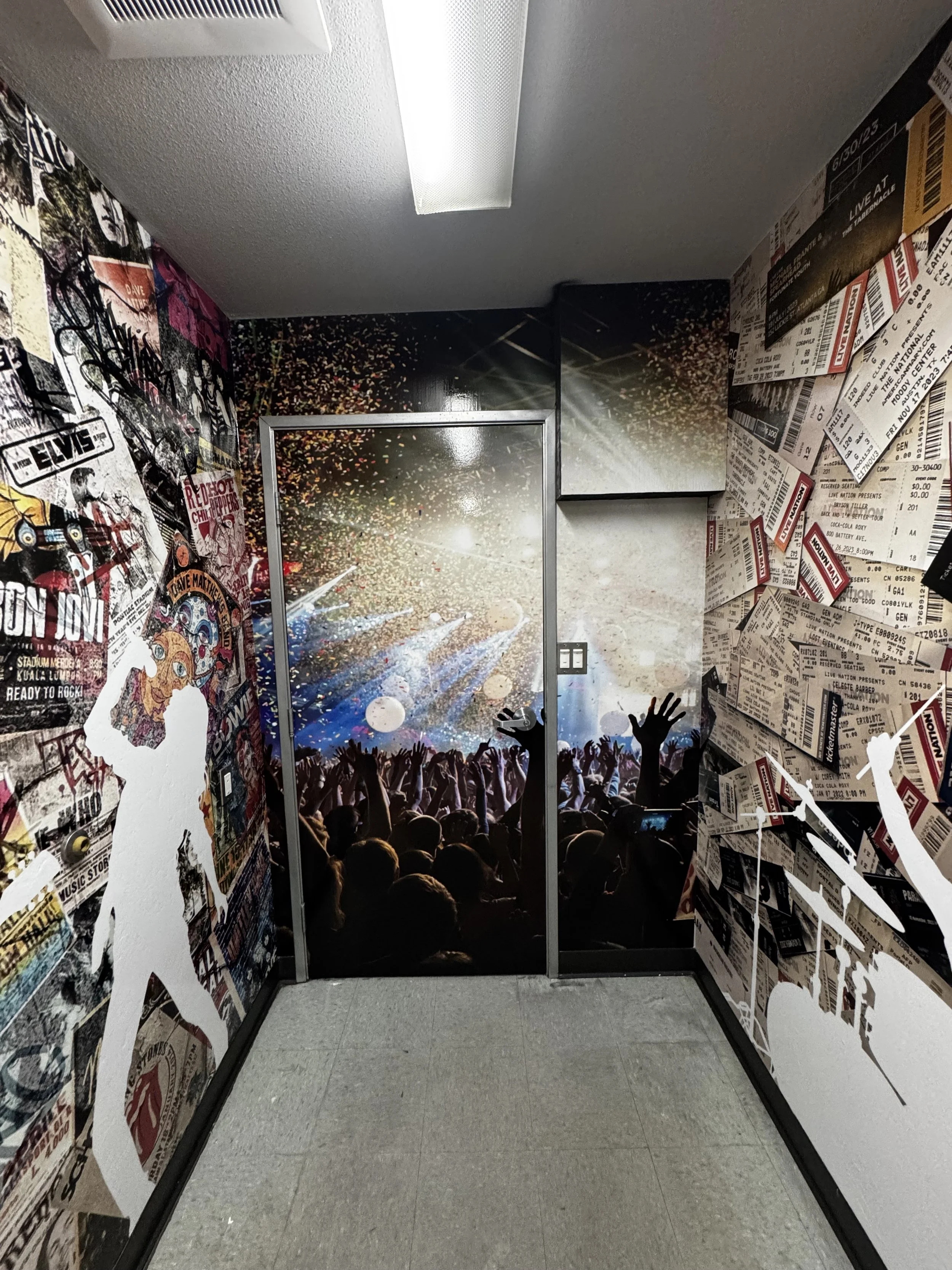 Hallway with concert scene wall art, including a crowd with raised hands, and murals of a woman, posters, and ticket stubs on the walls.