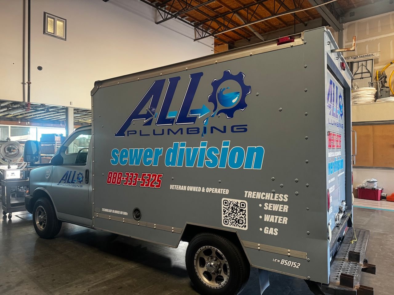 Service truck for All Plumbing, specializing in sewer division, parked inside a garage or warehouse. The truck features company logo, contact number, QR code, and services like trenchless sewer, water, and gas.