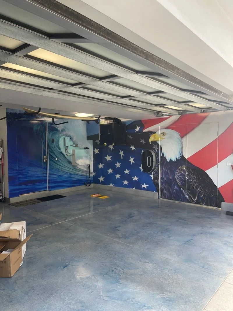Garage wall mural featuring a bald eagle in front of an American flag backdrop, with a wave scene on the adjacent wall.
