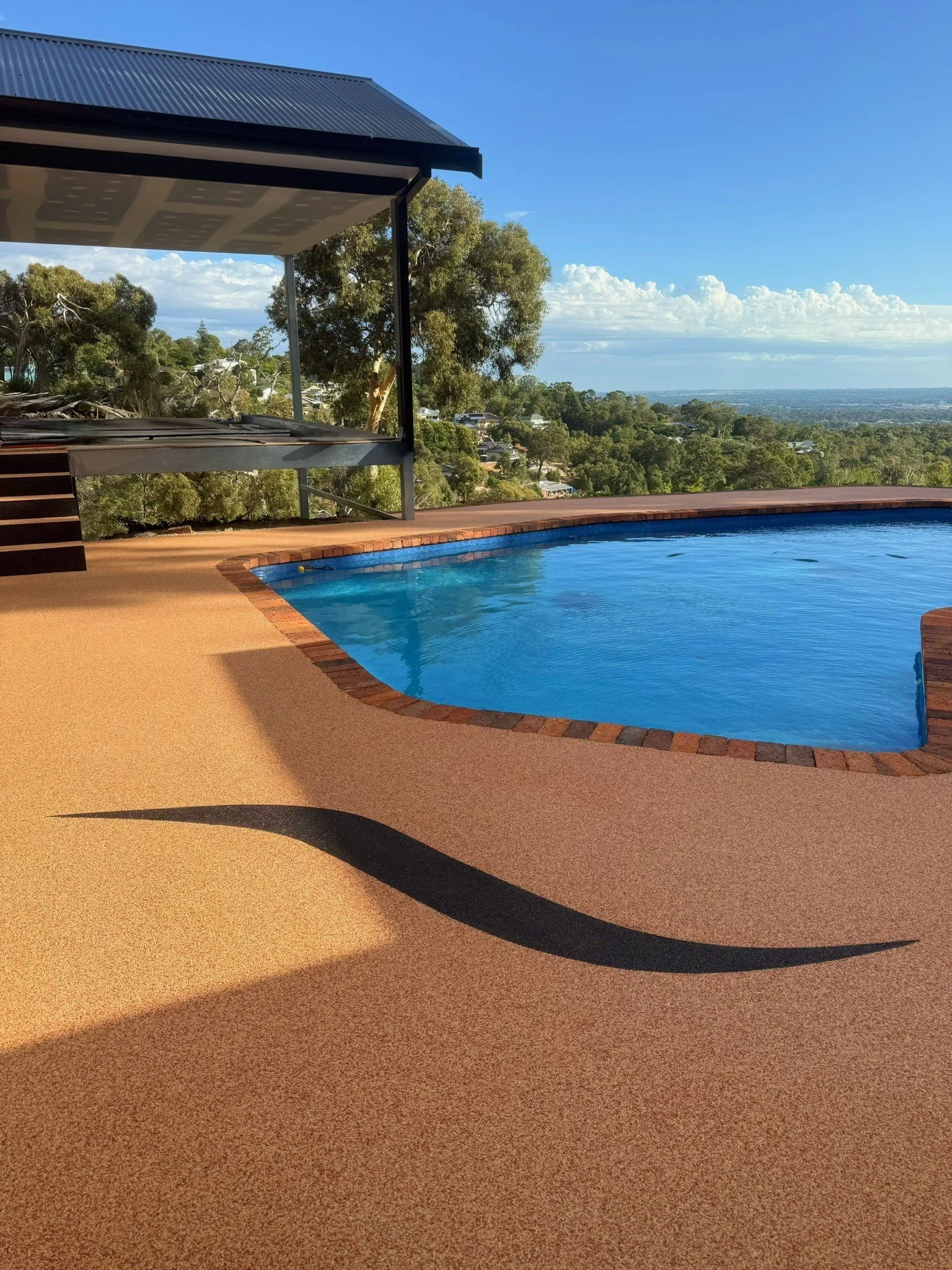 Perth outdoor pool area featuring permeable Vuba Resin surfacing with decorative wave design, bordered by brick edging and surrounded by lush landscaping and modern patio.
