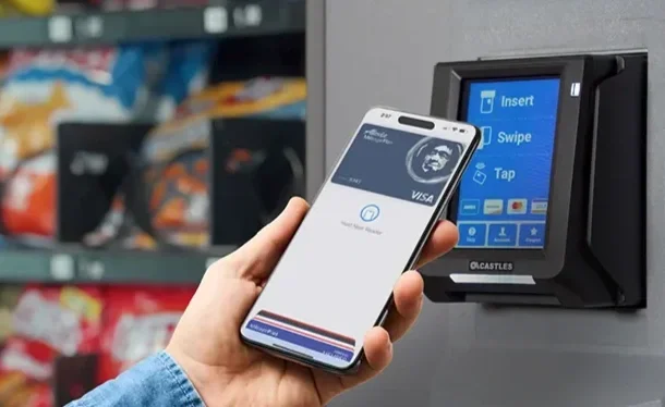 Person holding a smartphone near a card payment terminal in a convenience store.