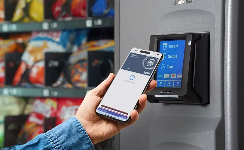 A person using a smartphone with a contactless payment app to pay at a vending machine.