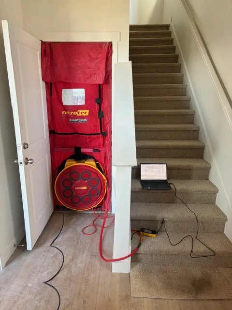 A fire escape plan and equipment stored behind a closet door near a staircase, with testing devices and cables on the floor.
