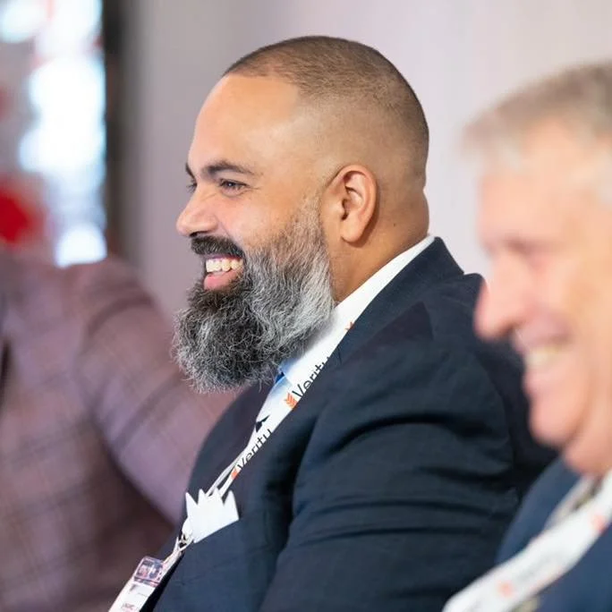 Two men in business suits sitting and smiling at a professional event.