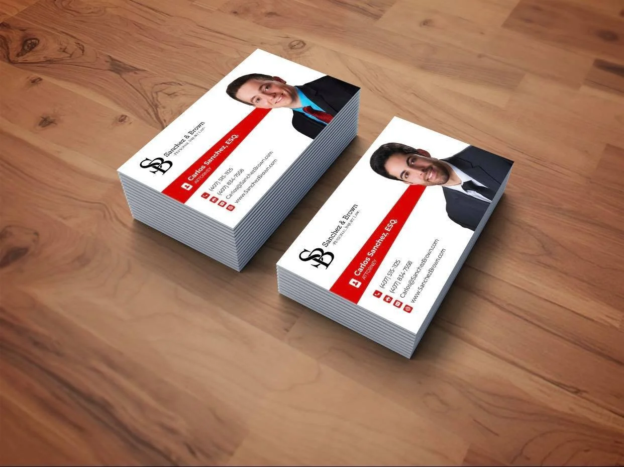 Stack of business cards featuring a photo of a man in a suit, with contact information and social media icons on a wooden surface.