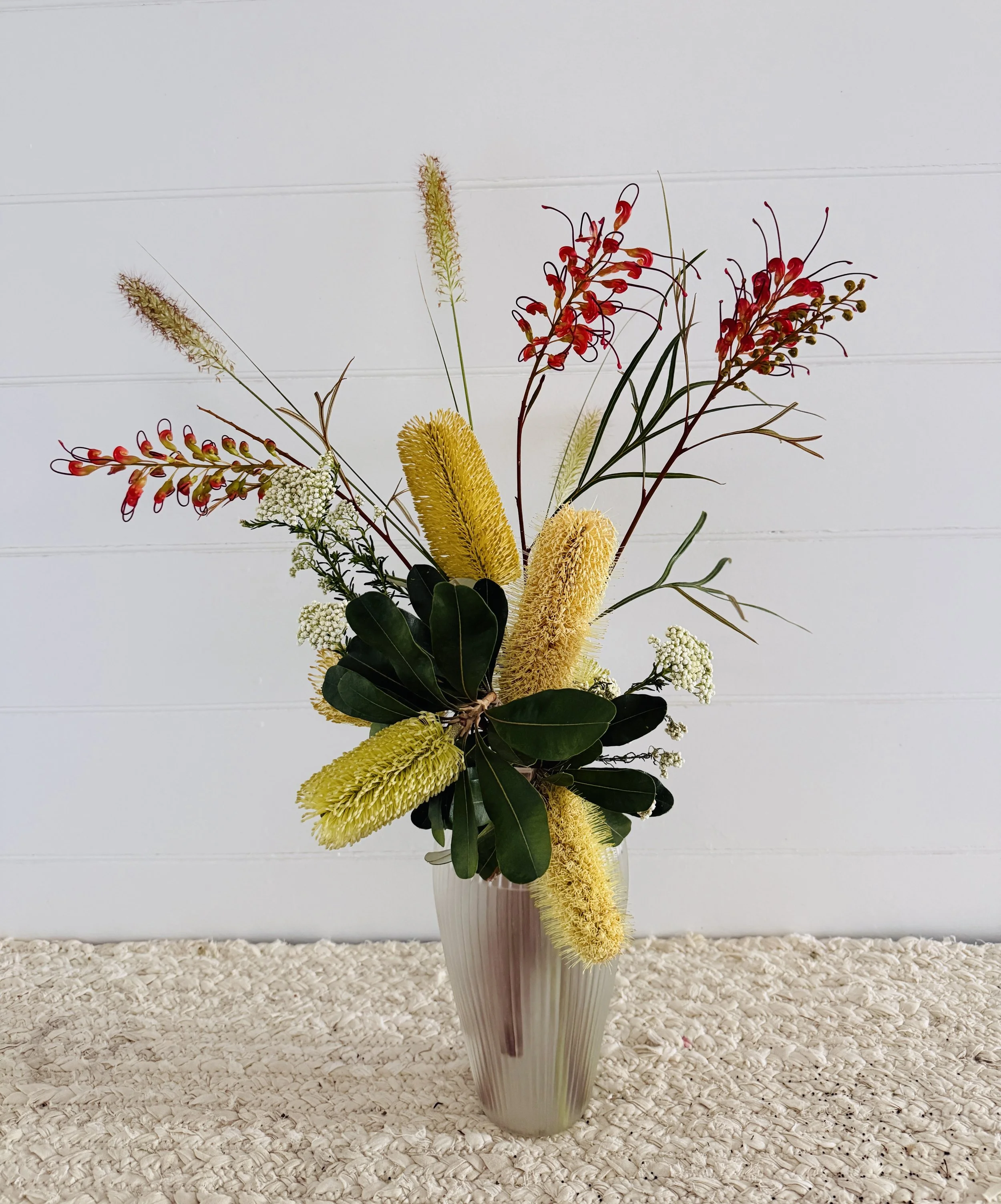 Australian native flower arrangement with yellow banksia, red grevillea, white rice flowers and native grass.