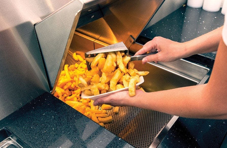 Person using tongs to put cooked French fries into a container from a commercial deep fryer. Radlett Fish & Chips, Grill