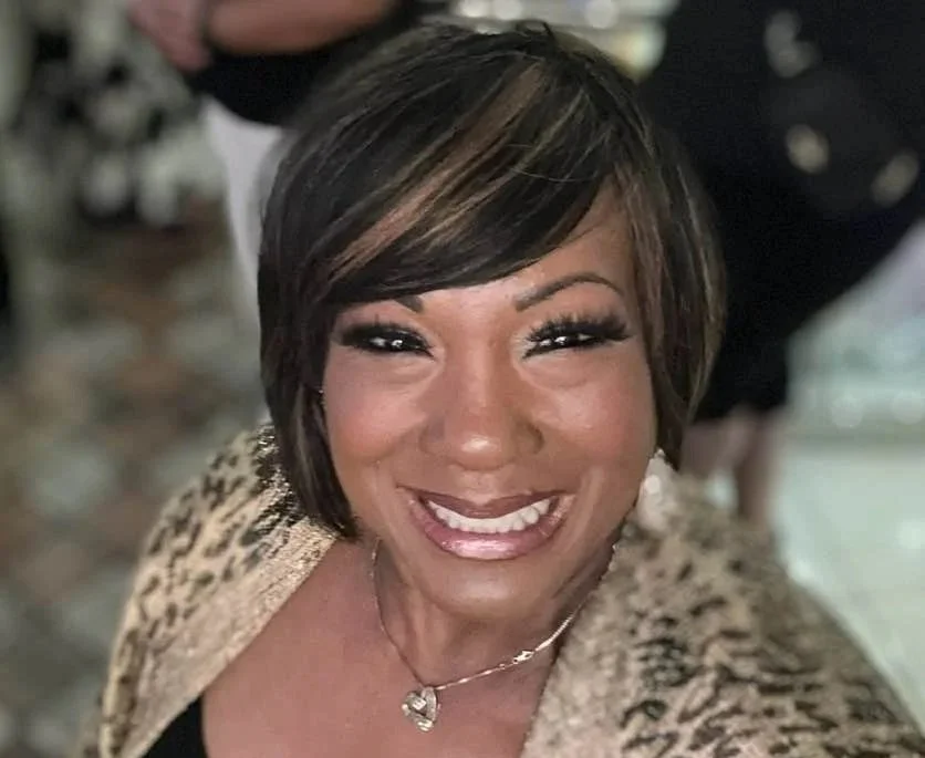 A woman with short dark hair and highlights, smiling and wearing a leopard print jacket and a necklace.