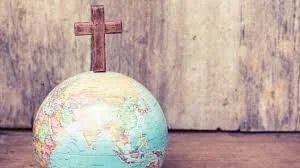 A globe with a Christian cross on top, placed on a wooden surface.