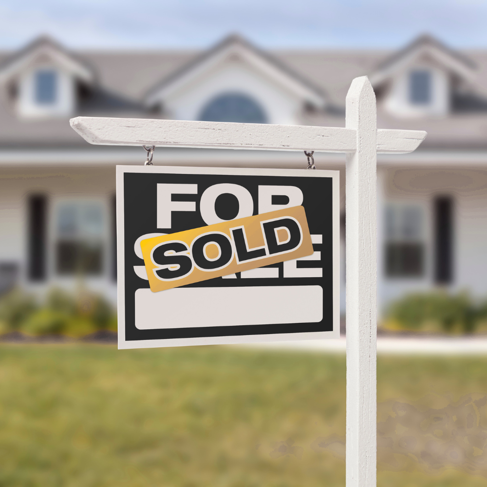Real estate 'For Sale' sign with a 'Sold' overlay in front of a suburban house with a blurred background.