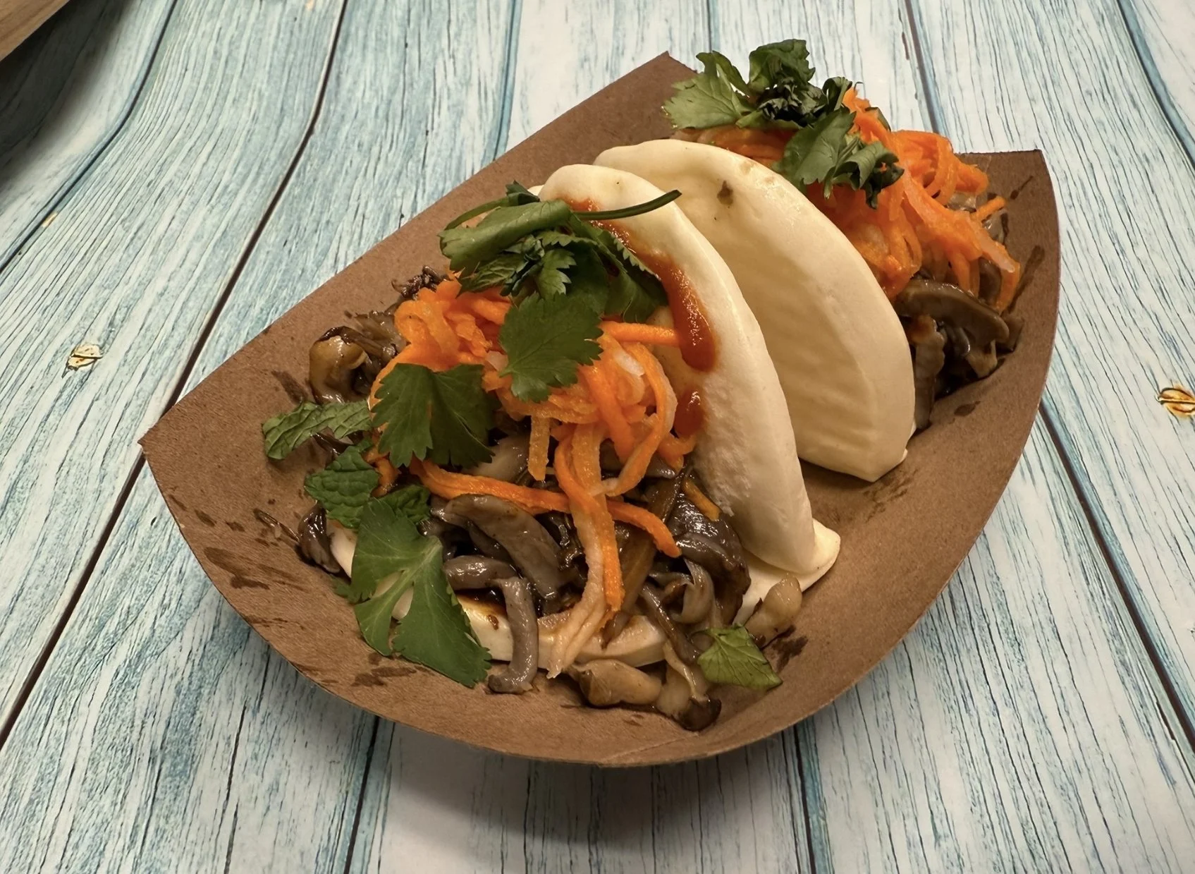 Two steamed bao buns filled with sautéed mushrooms, shredded carrots, and fresh cilantro on a rustic wooden table.