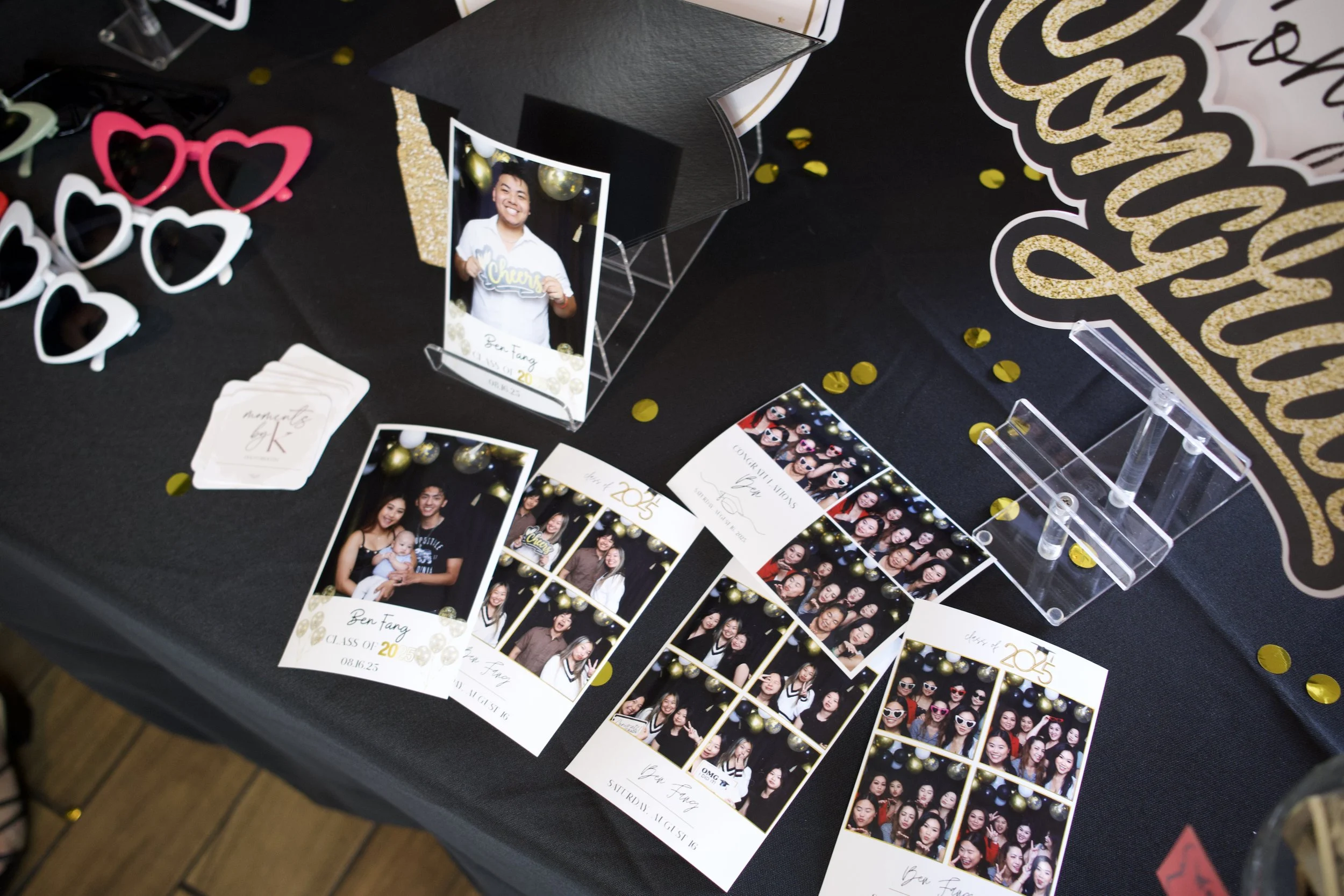 Photo booth display with photo strips and props at a celebration event, decorated with gold and black accents.