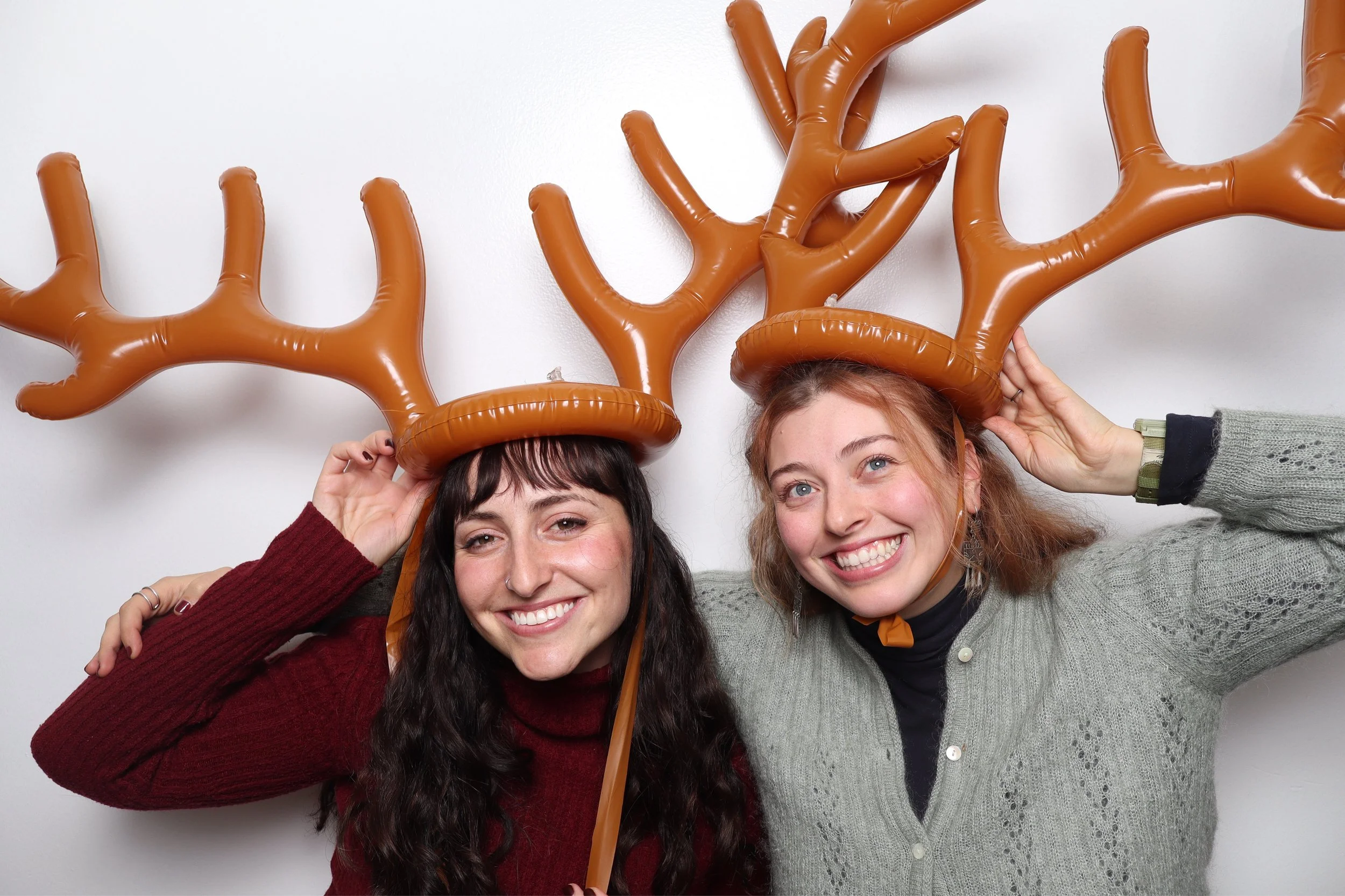 Two women smiling and wearing reindeer antler hats made of brown balloons.