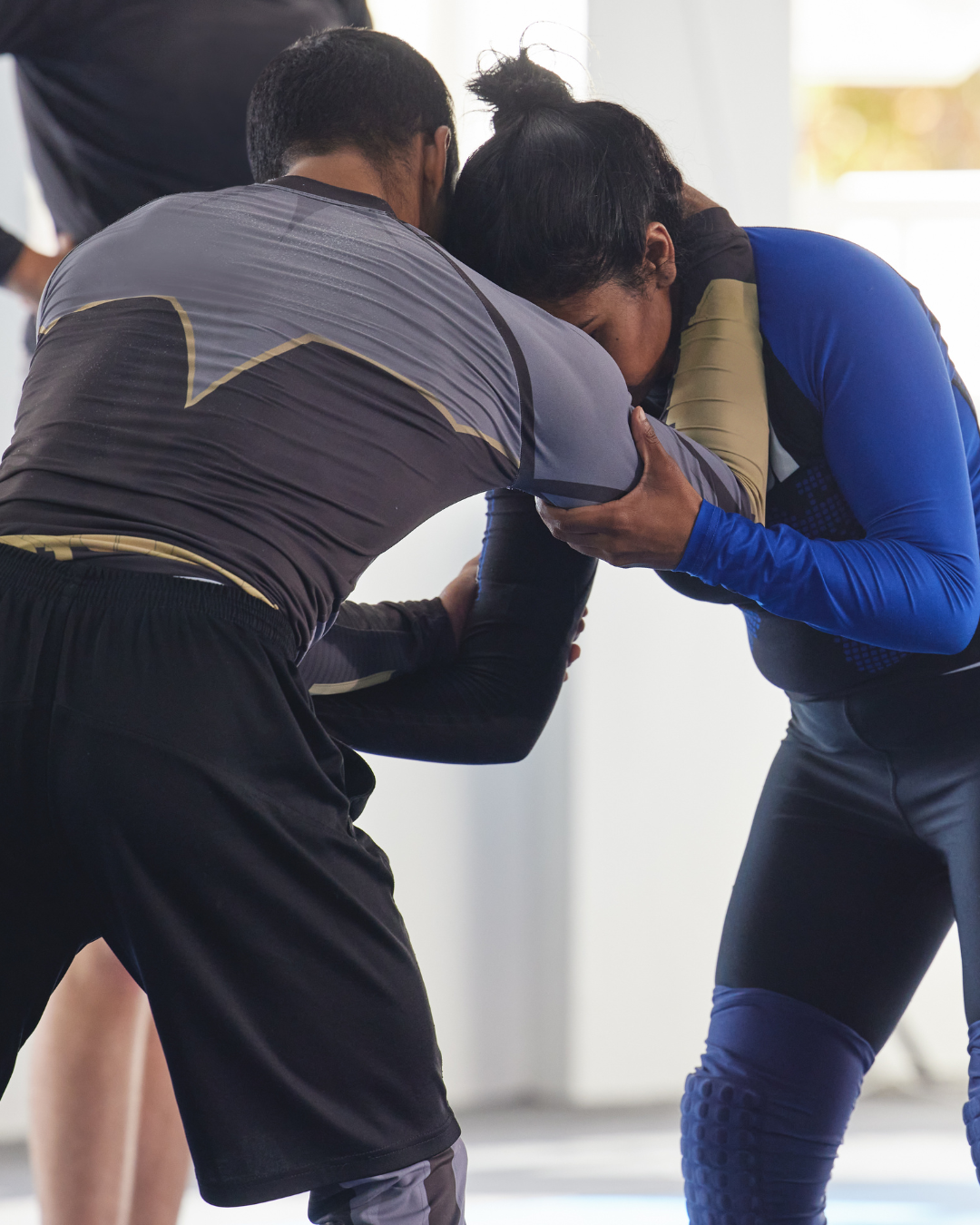 Two people training in a wrestling or grappling move, with one person leaning forward and gripping the other around the neck while the other person counters.